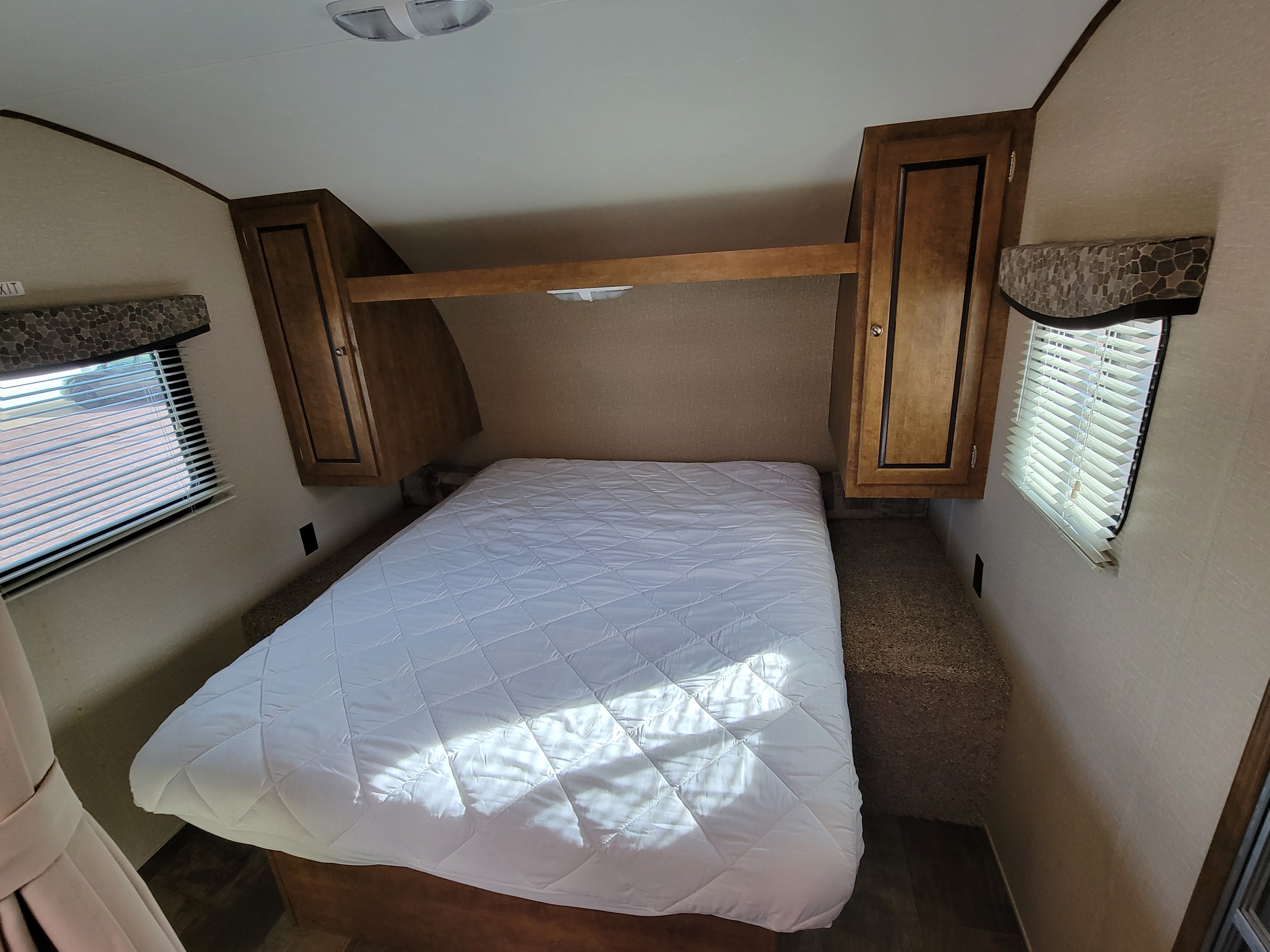 Clean RV rental bedroom featuring a white quilted bed, ample overhead storage, and window blinds.. Crossroads RV Z-1 2015