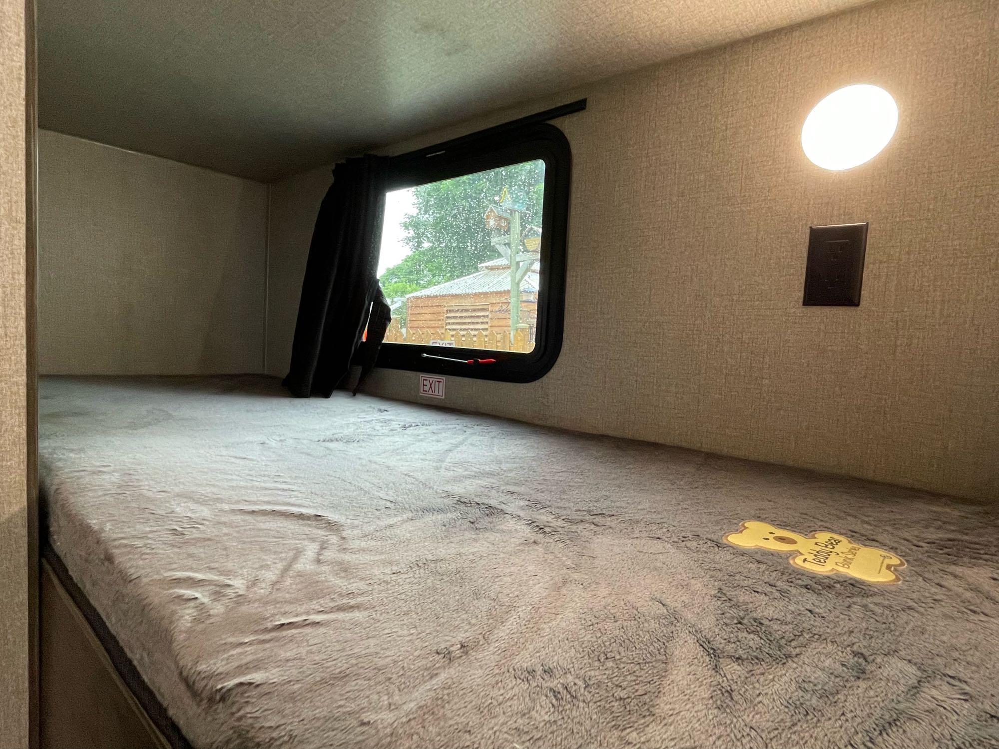 Cozy RV rental bunk bed with a plush grey mattress, window view, reading light, and "Teddy Bear Bunk Series" label.. Jayco Flight 2021