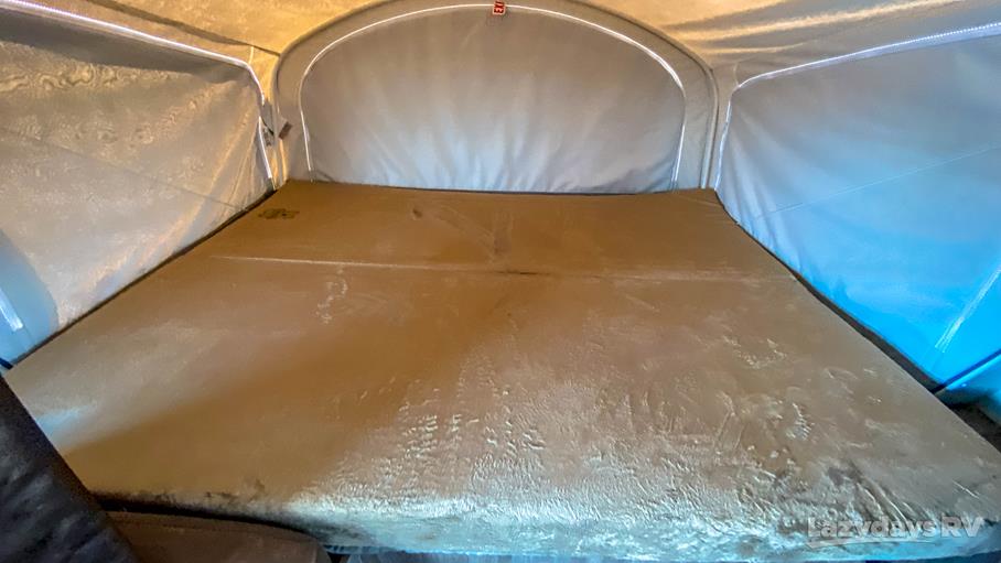 Spacious bed inside an RV rental pop-up camper, featuring light brown mattress, canvas walls, and an EXIT sign.. Jayco Jay Feather 2018
