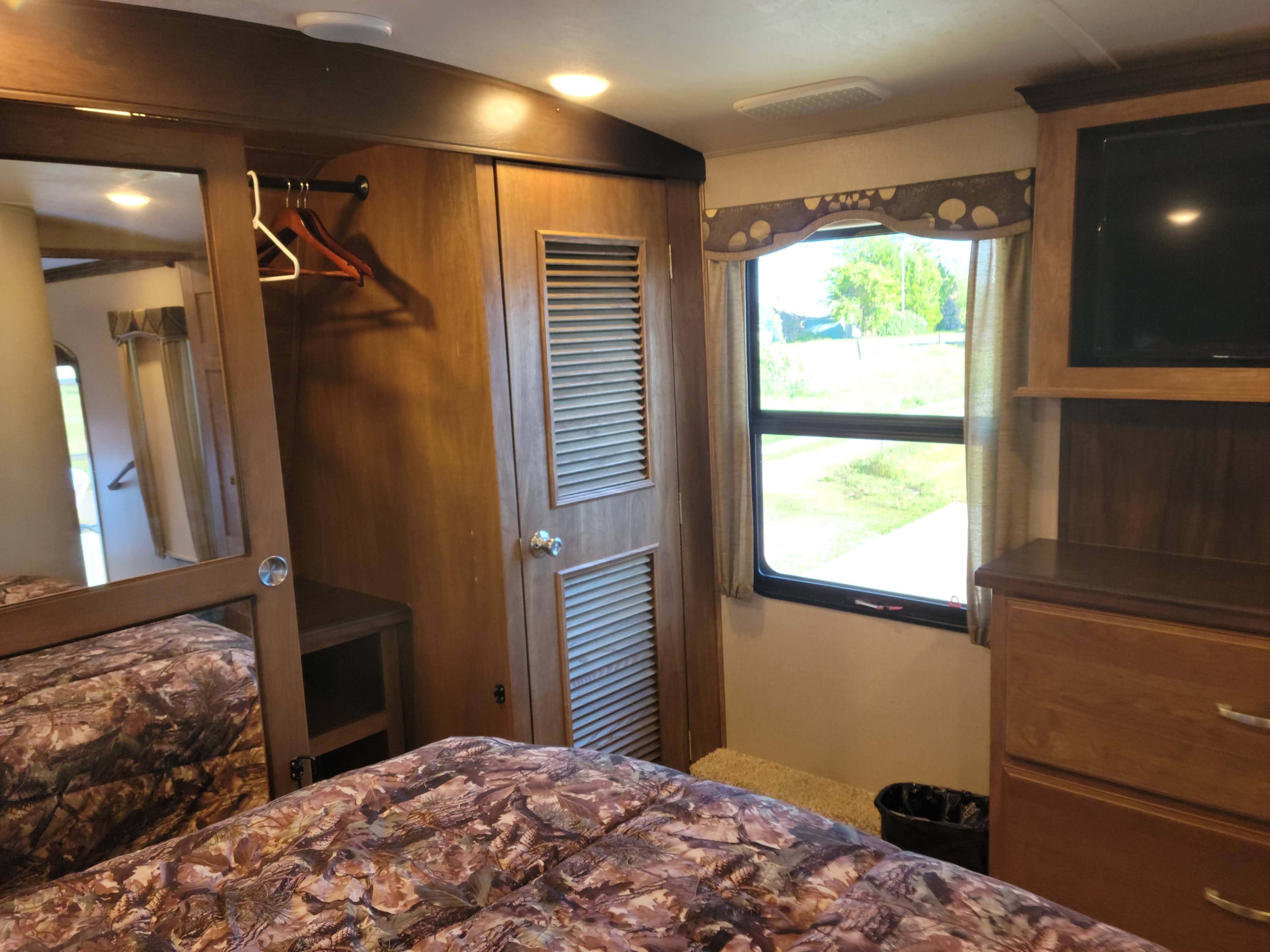 Cozy RV rental bedroom featuring a bed, mirrored closet, window, and entertainment area with a TV.. Keystone Montana 2017