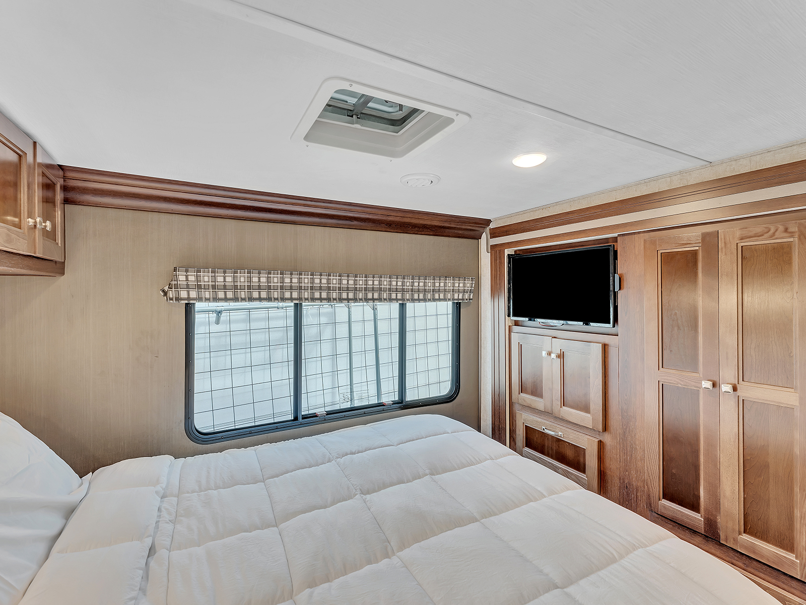 An RV rental bedroom showing a comfortable bed with white bedding, a window, wall-mounted TV, and wooden storage.. Forest River Sunseeker 2020