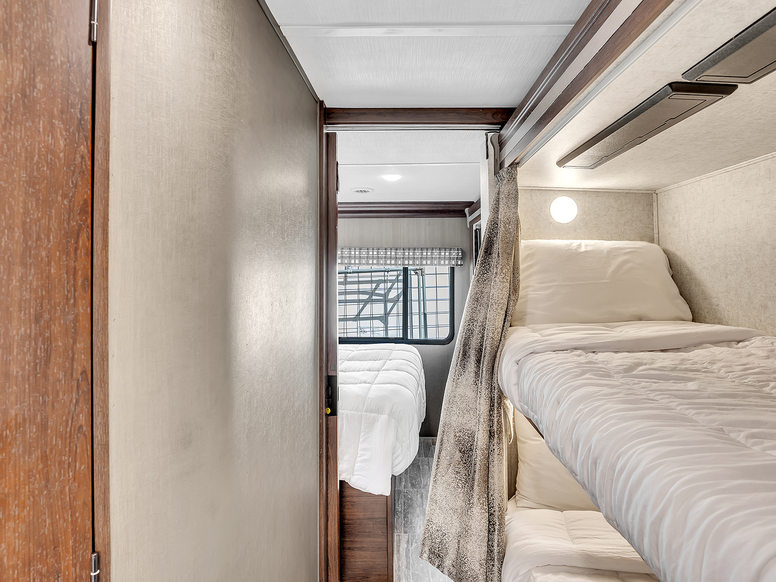 Comfortable bunk beds in an RV rental, featuring white bedding and a privacy curtain next to an additional bedroom.. Forest River Sunseeker 2020