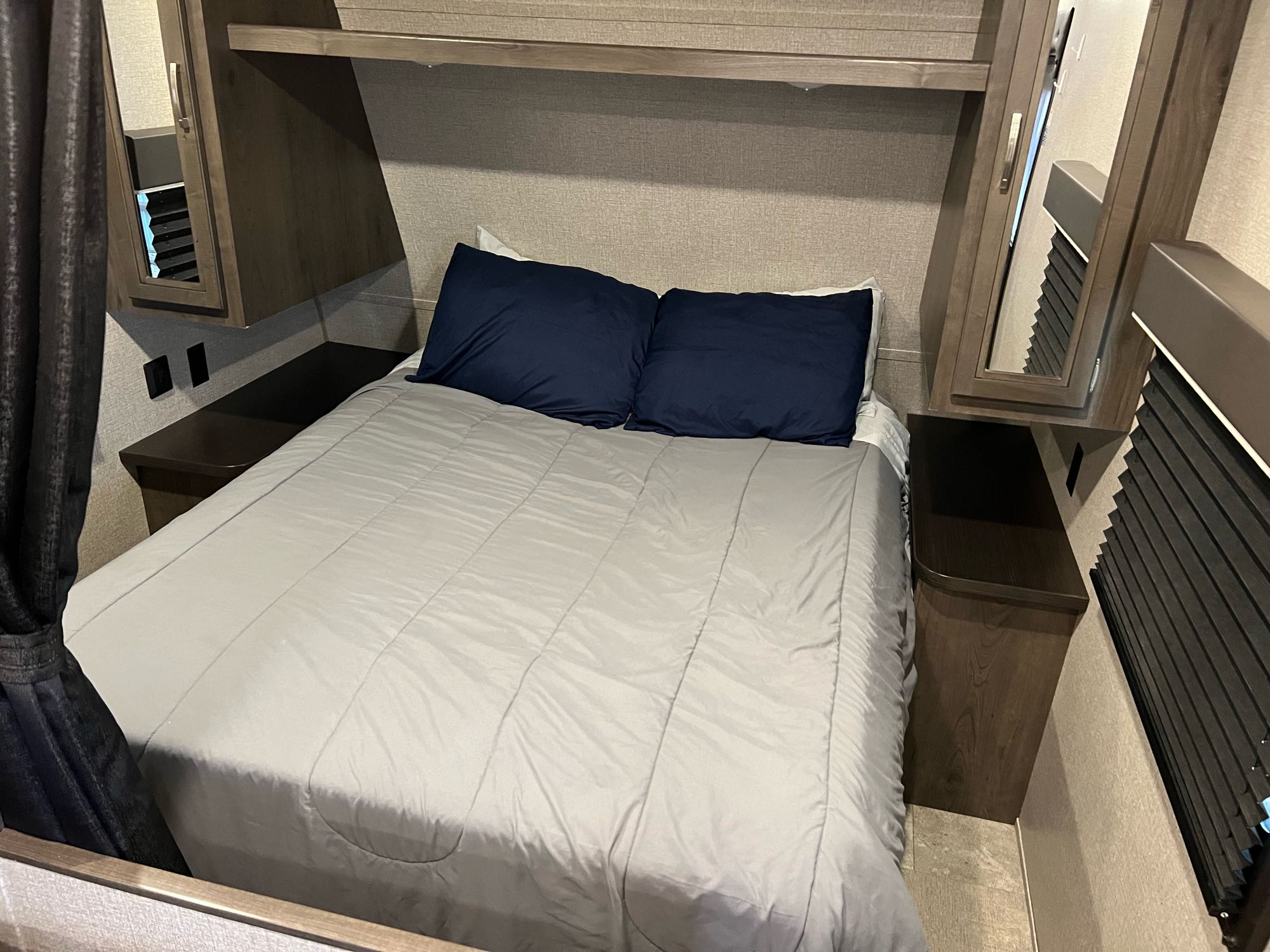 Inside an RV rental bedroom: gray comforter, blue pillows, integrated nightstands, and overhead cabinets.. Jayco Jay Flight 2021