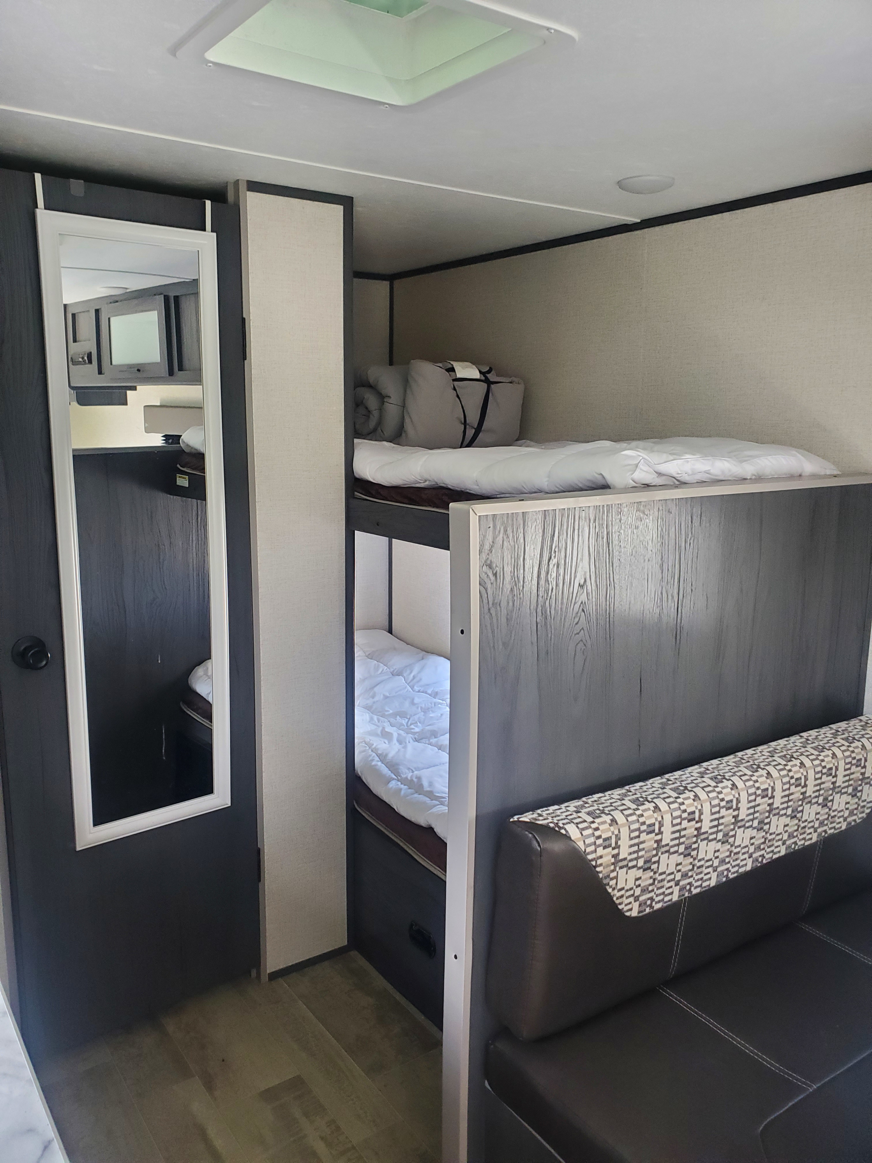 Inside an RV rental: view of bunk beds with bedding, a full-length mirror on a door, and a comfortable seating area.. Aspen Trail LE 2021
