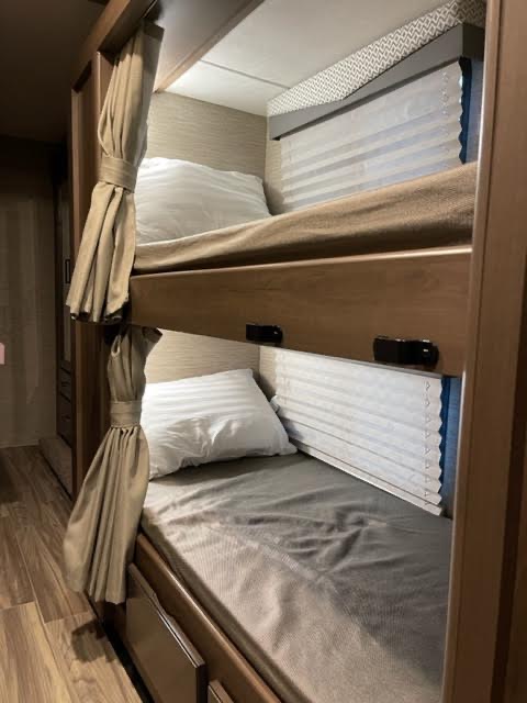 Compact RV rental bunk beds with pillows, sheets, and privacy curtains, ideal for family travel.. Thor Four Winds 2022