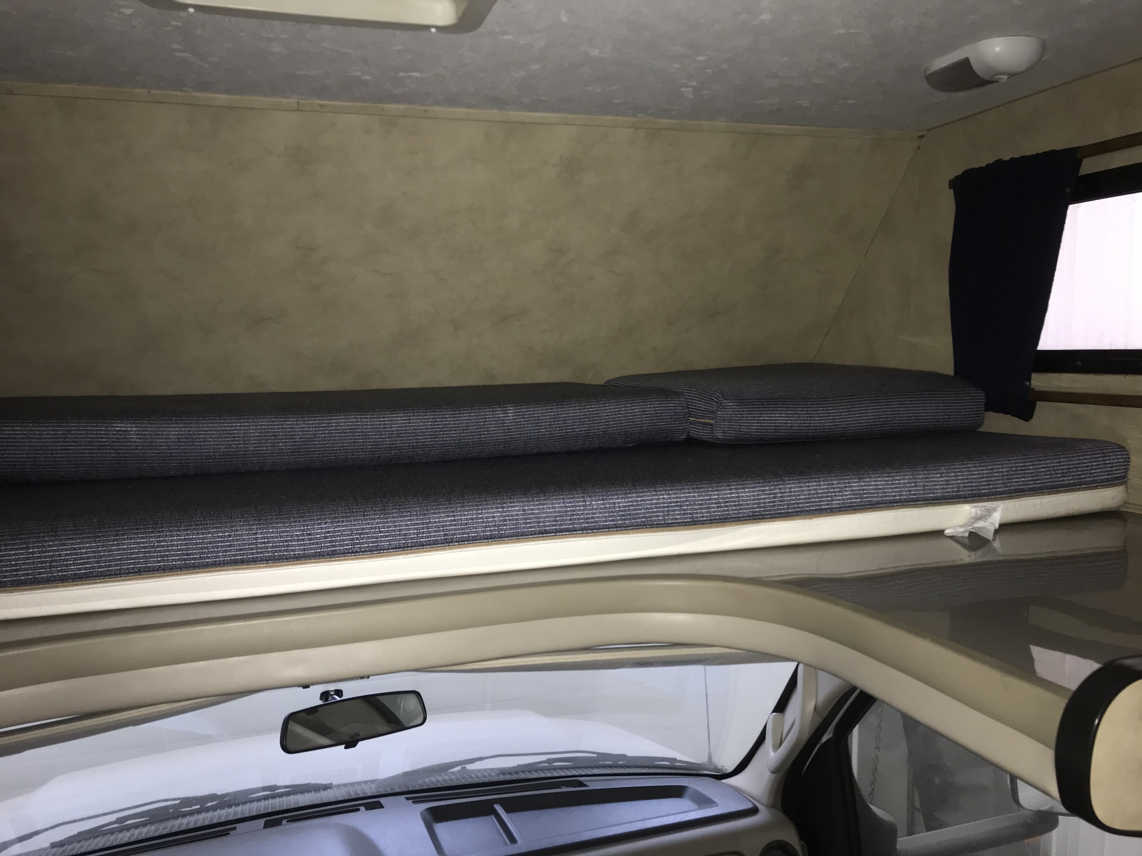 Inside an rv rental: A view of the comfortable cab-over bunk with blue striped mattresses, positioned above the vehicle's dashboard.. Thor Motor Coach Majestic 19G 2018
