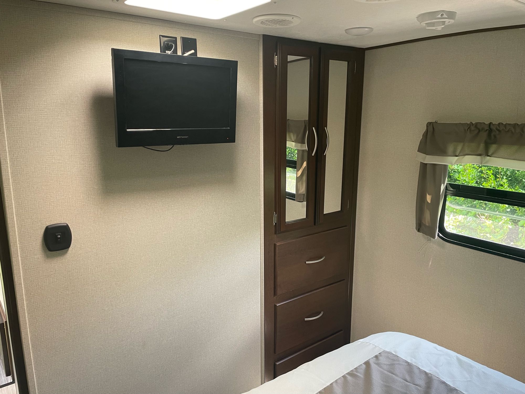 Inside an RV rental, a cozy bedroom features a wall-mounted TV, wardrobe, and window view.. Prime Time Crusader 2018