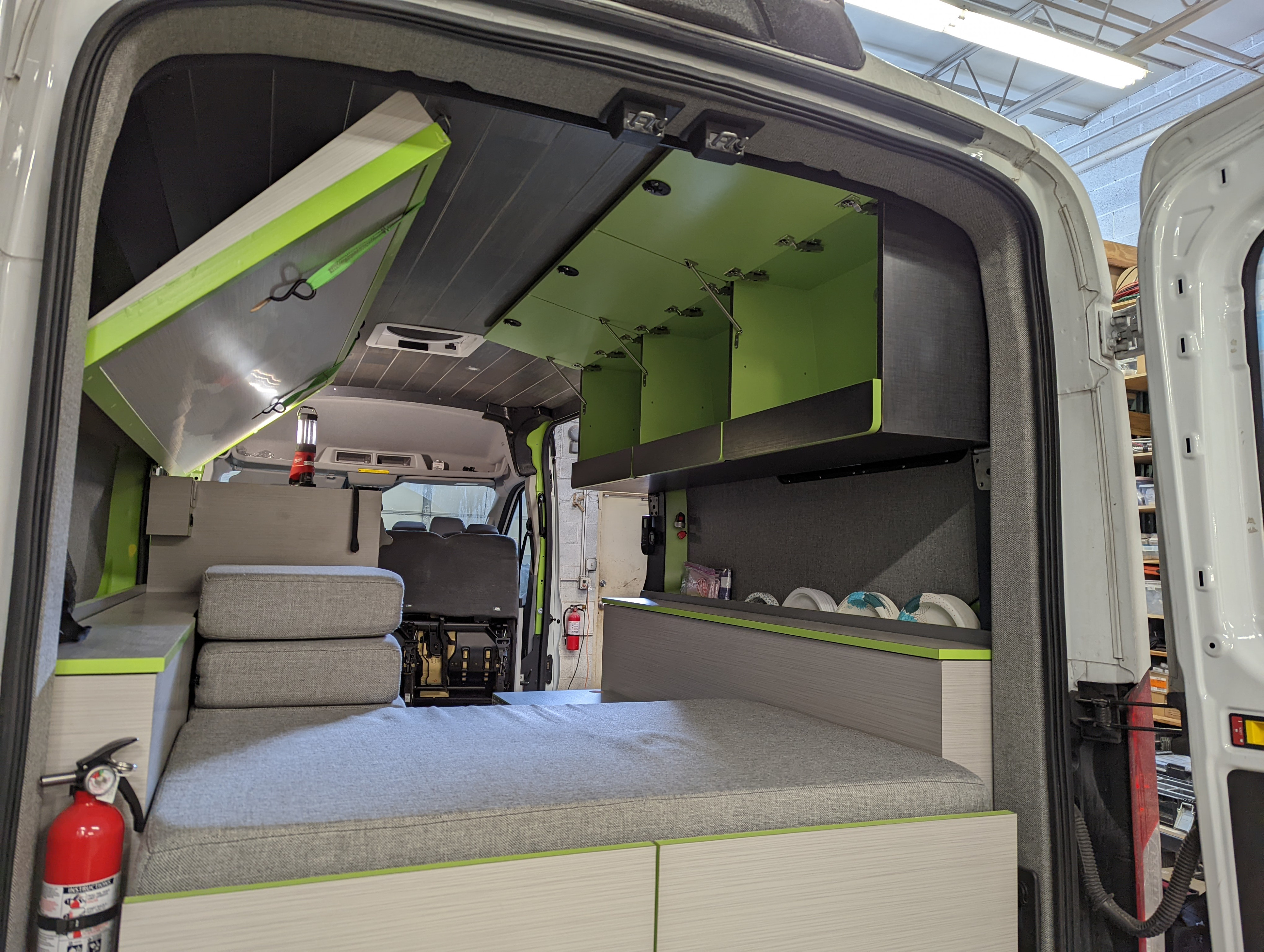 Inside a sleek RV rental camper van: a cozy bed, open lime green storage cabinets, and smart built-ins for adventures.. Ford Transit 2018