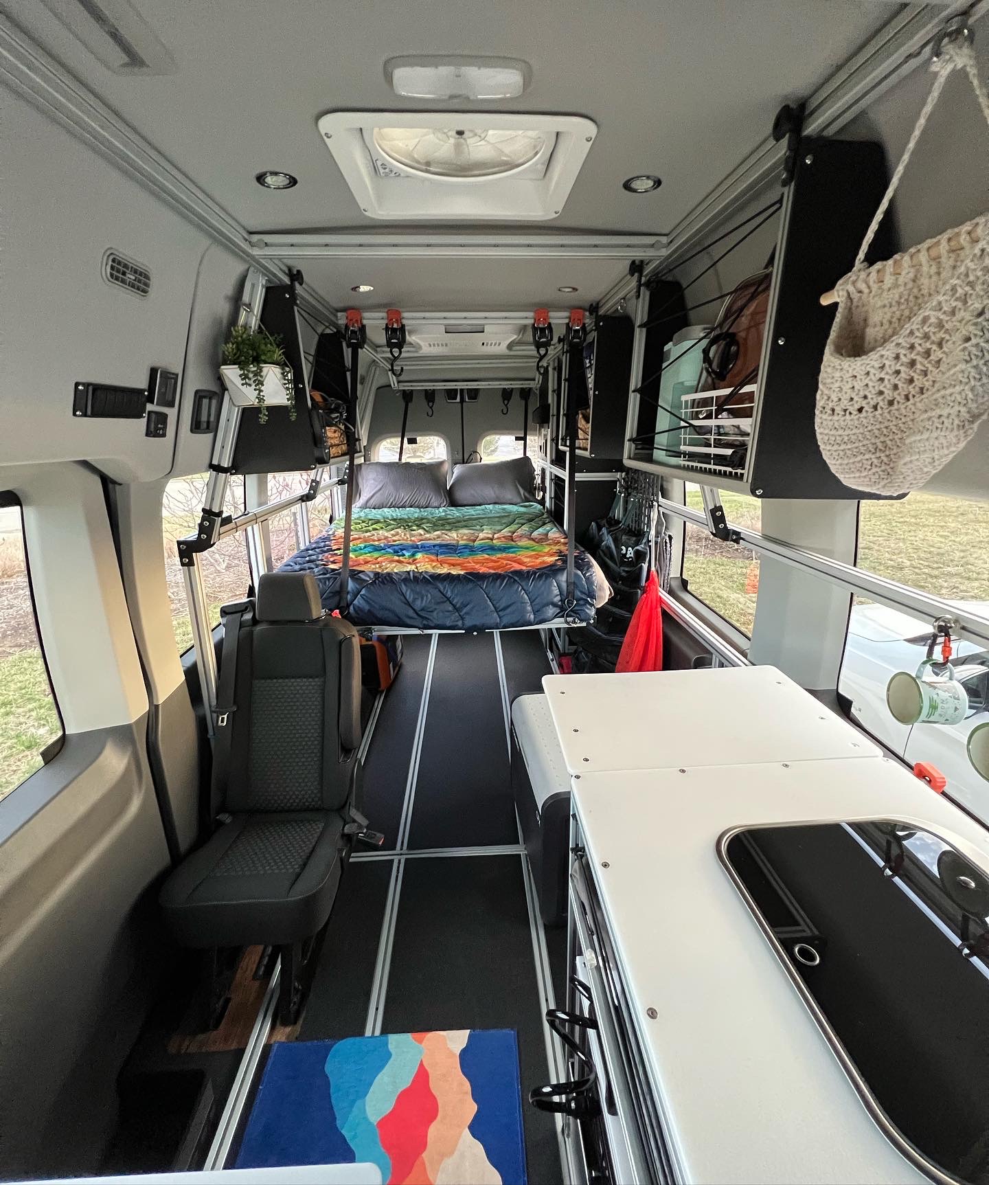 Organized camper van interior with cozy bed, passenger seat, & custom kitchenette. Ready for your next rv rental road trip!. Ford Transit 2020