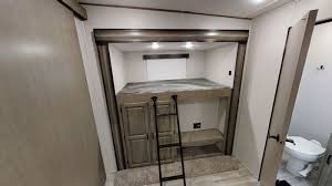 This RV rental's cozy bunk room features a ladder to an upper bed, storage below, and an adjacent bathroom, ideal for family travel.. Coachmen Chaparral 2021