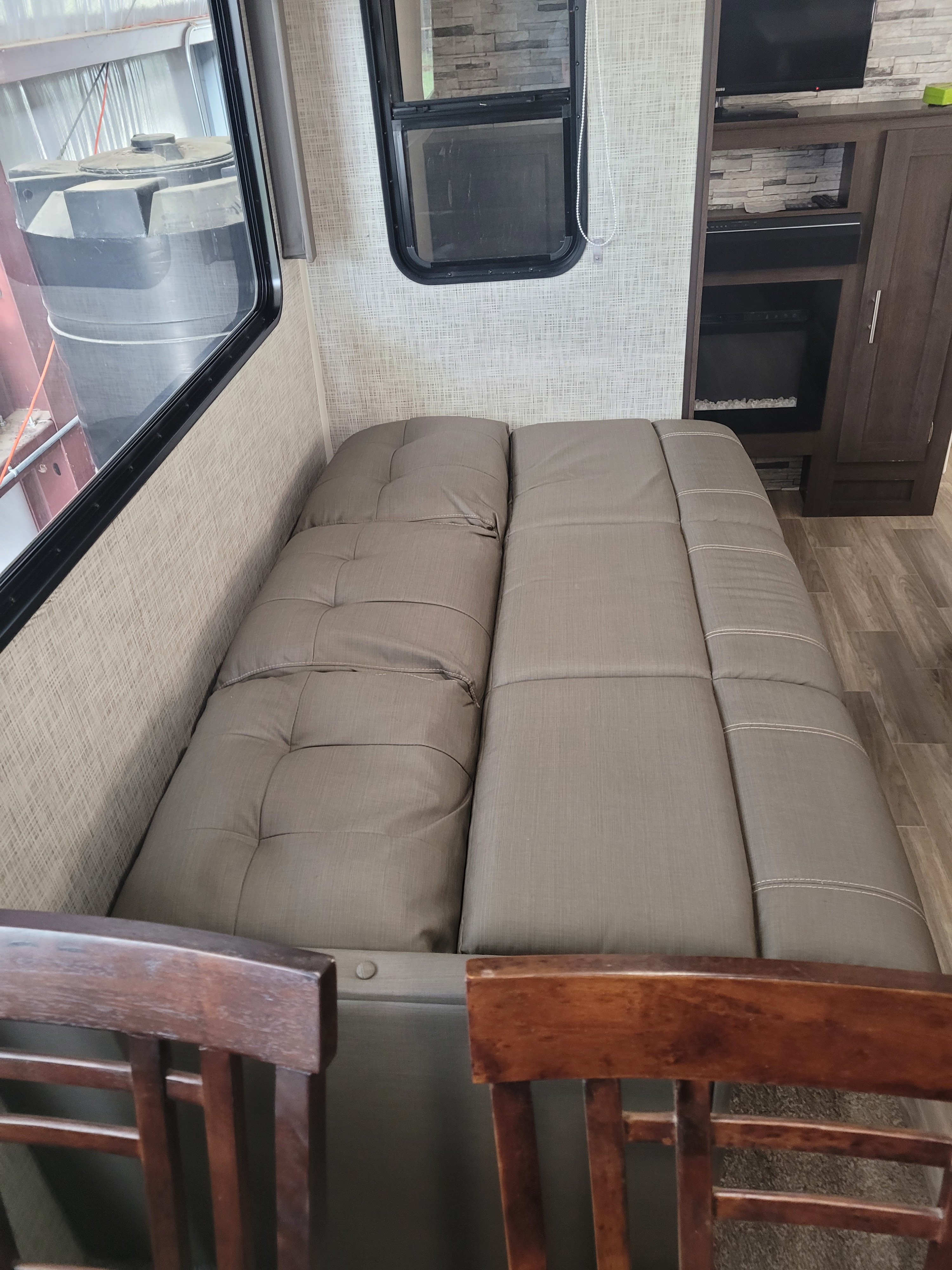 RV rental interior: cozy convertible bed/dinette, window view of tank, entertainment cabinet, and wood-look floor.. Forest River Wildwood 2020