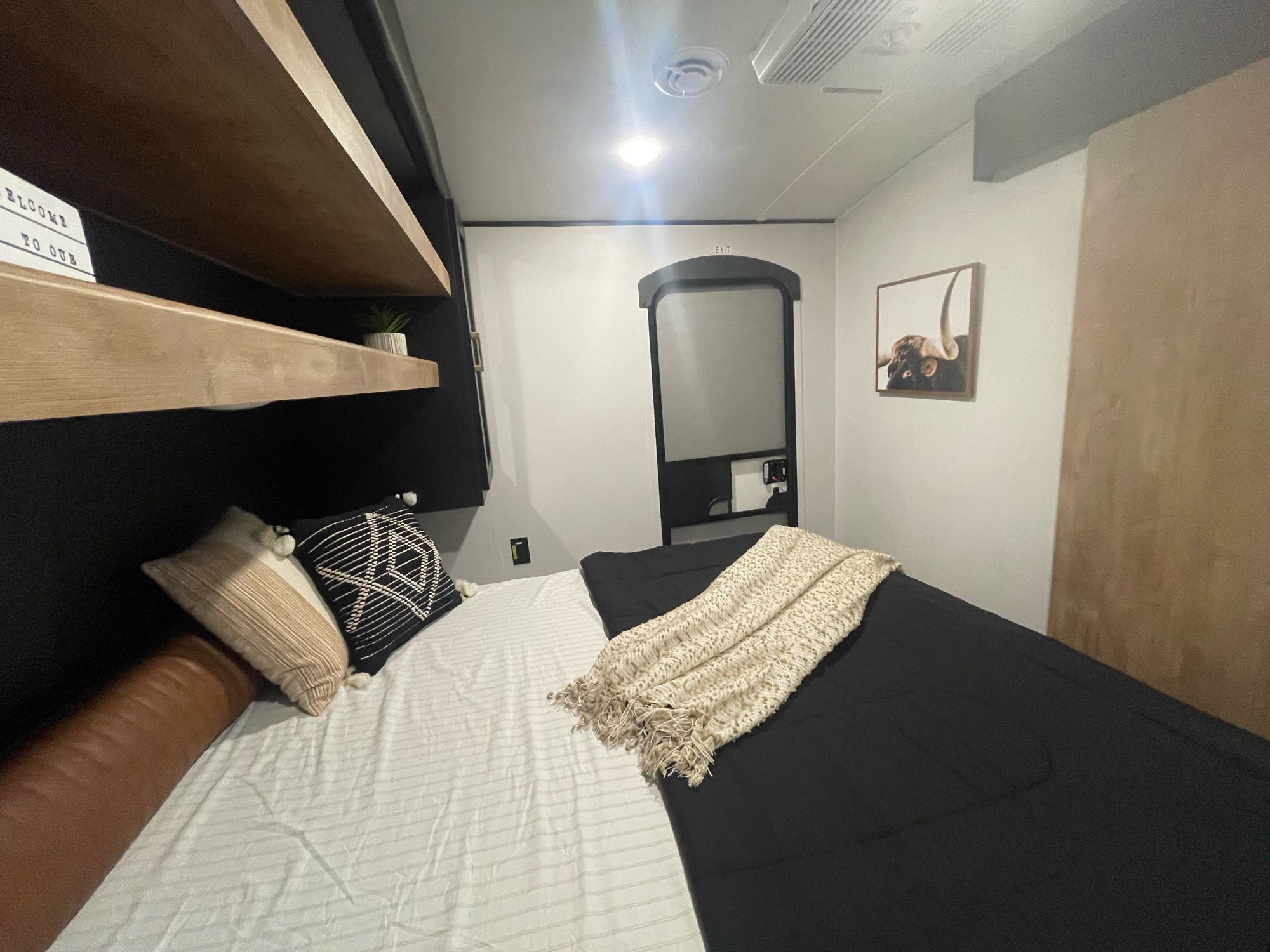 Step into this modern RV rental bedroom featuring a comfy bed, floating shelves, and an exit door. A cozy, well-appointed space.. Keystone Springdale 2022