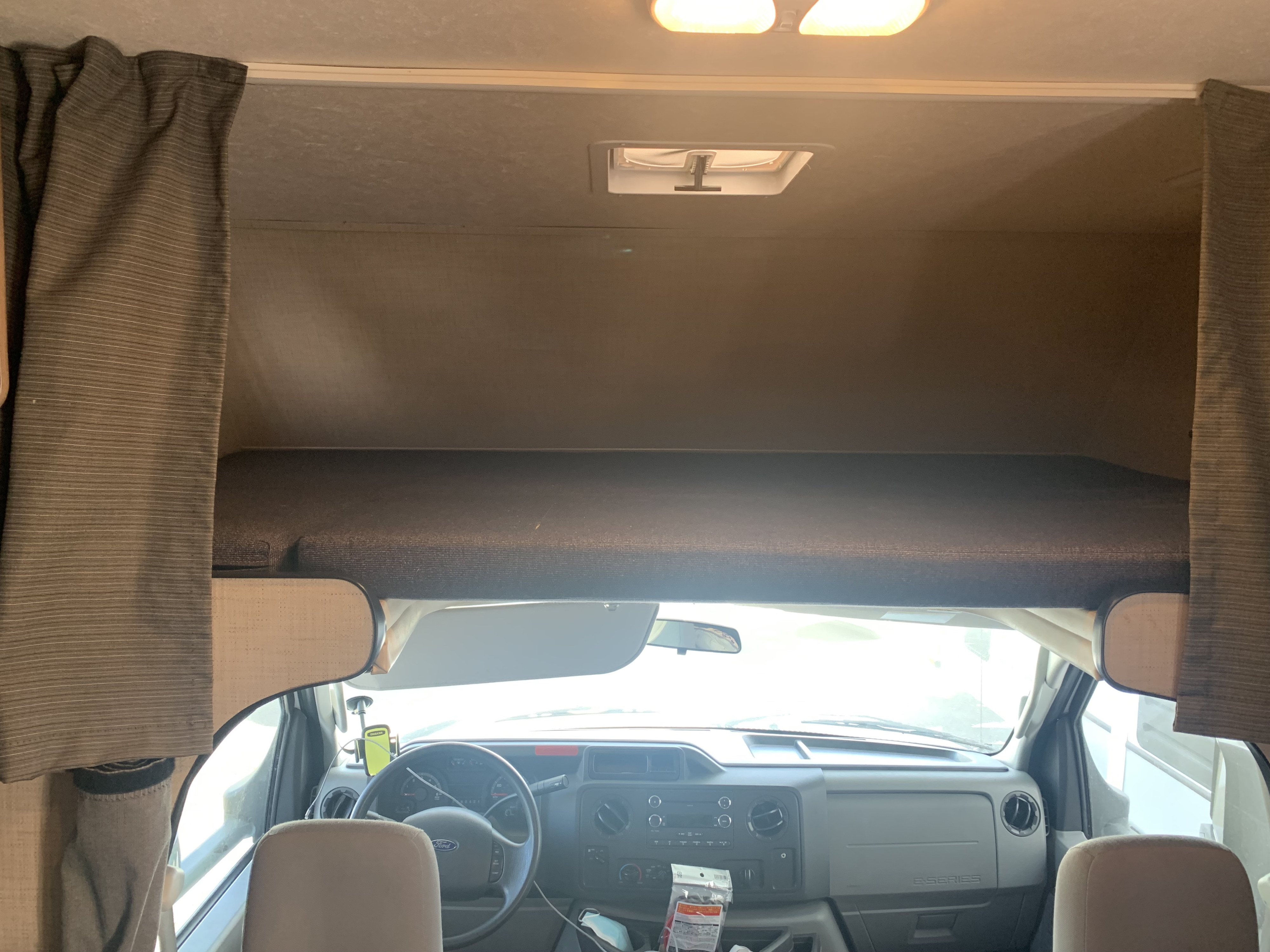 RV rental interior: view of the driver's cab, steering wheel, dashboard, and the bunk above.. Thor Majestic 2018