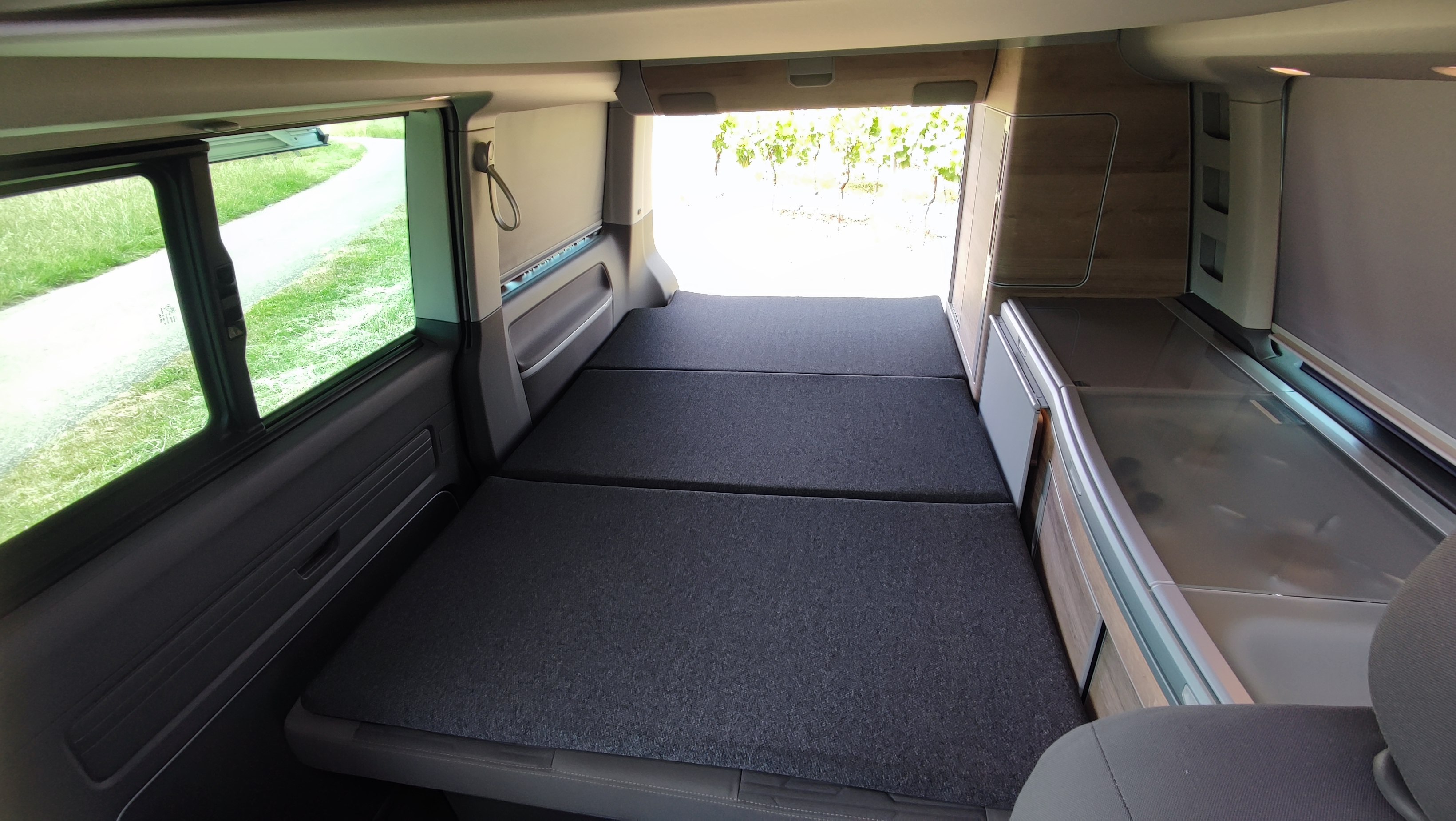 Inside an RV rental: view of the unfolded bed, compact kitchen area, and scenic path/vineyard through windows. Ready for adventure!. Volkswagen CALIFORNIA 2022