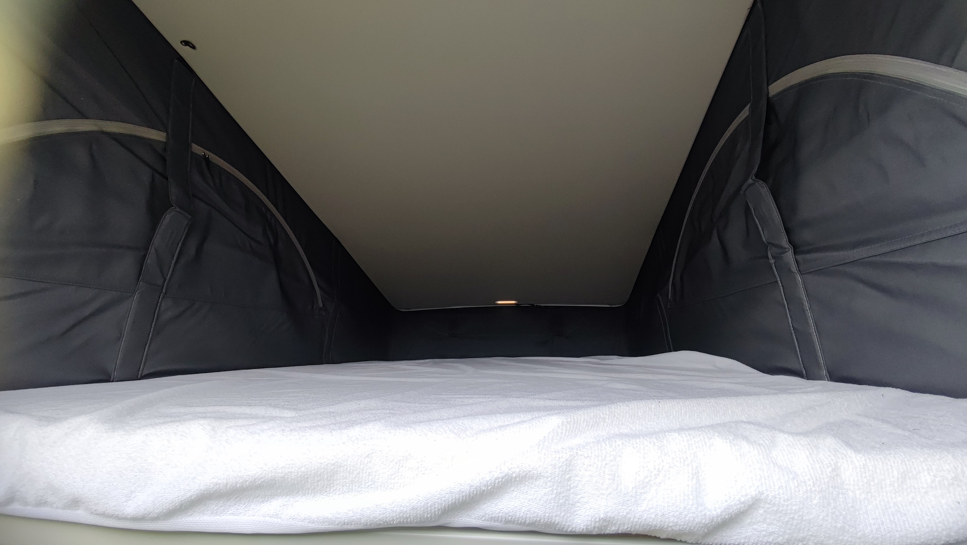 Cozy pop-top bed in an RV rental, featuring a white sheet and dark fabric tent walls, ideal for sleeping.. Volkswagen CALIFORNIA 2022