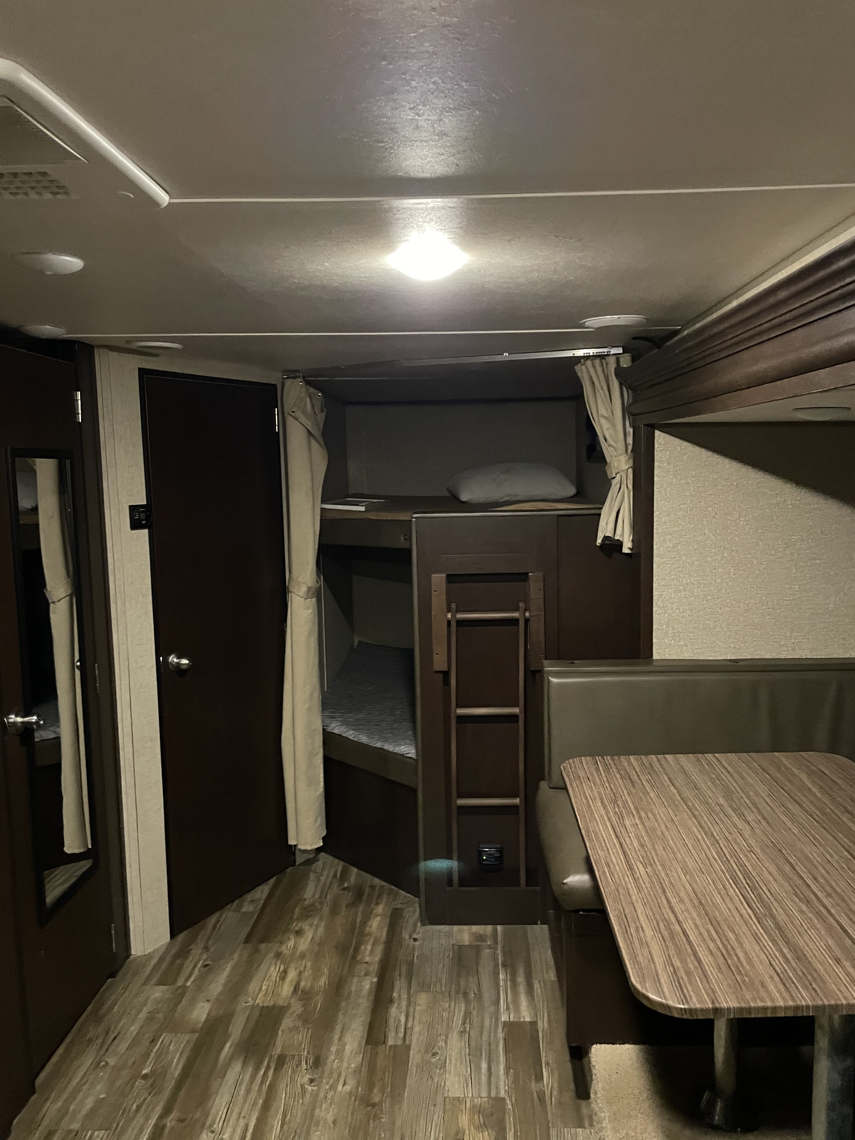 Inside an **rv rental** showing bunk beds with privacy curtains & ladder, plus a wooden table & booth seating for dining.. Forest River Cherokee Grey Wolf 2016