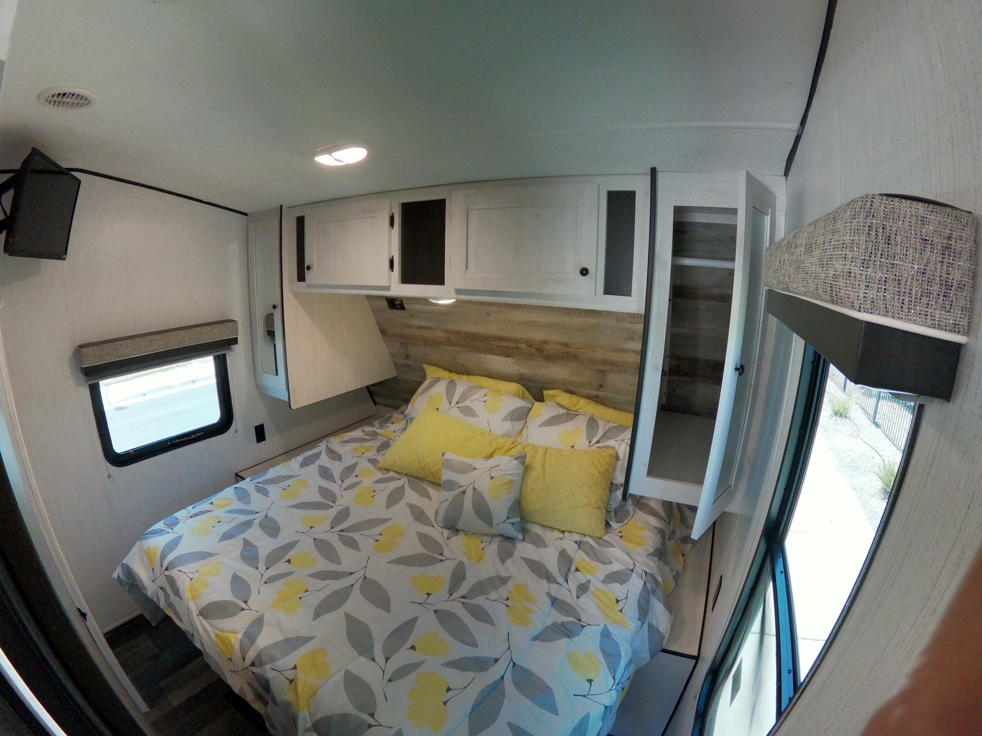 Step into a comfortable RV rental bedroom, featuring a cozy bed with floral bedding, yellow pillows, and overhead storage.. Heartland Lithium 2414 2021