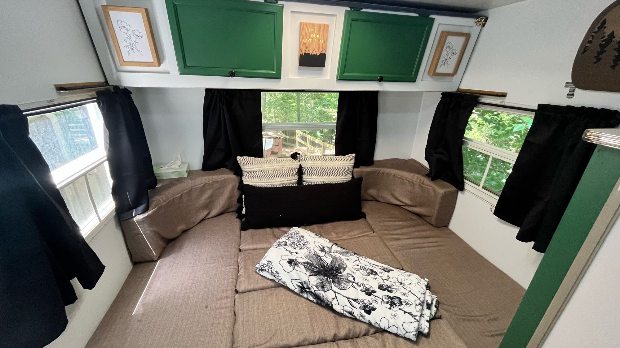 Cozy RV rental interior featuring a bed with brown cushions, green cabinets, and windows with black curtains. Ideal for a comfortable stay.. Aerolite Fifth Wheel 1998