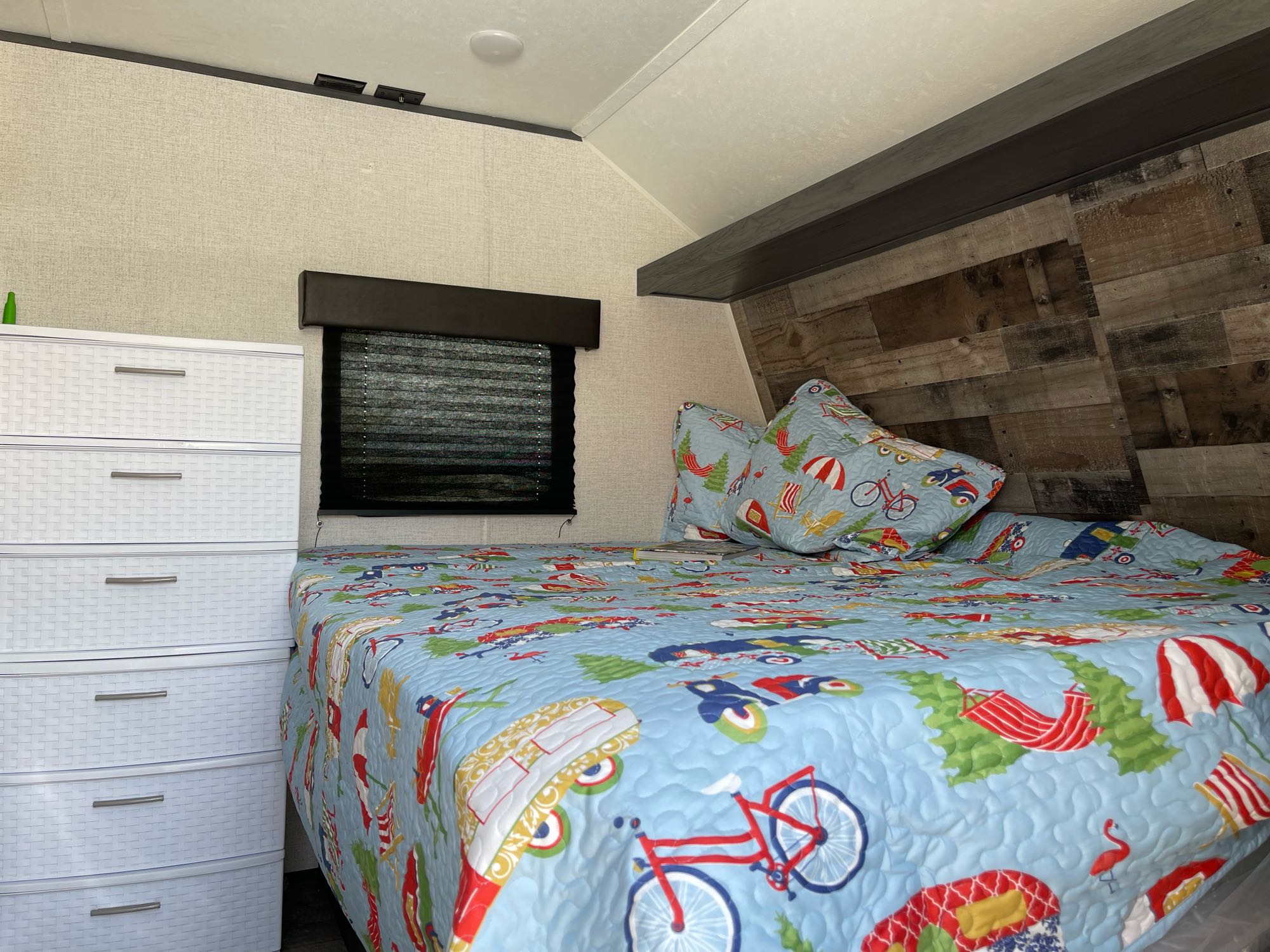 Cozy RV rental bedroom with a vibrant patterned quilt, white dresser, and wood-paneled accents. Ideal for travel.. Dutchmen Aspen Trailer 2021