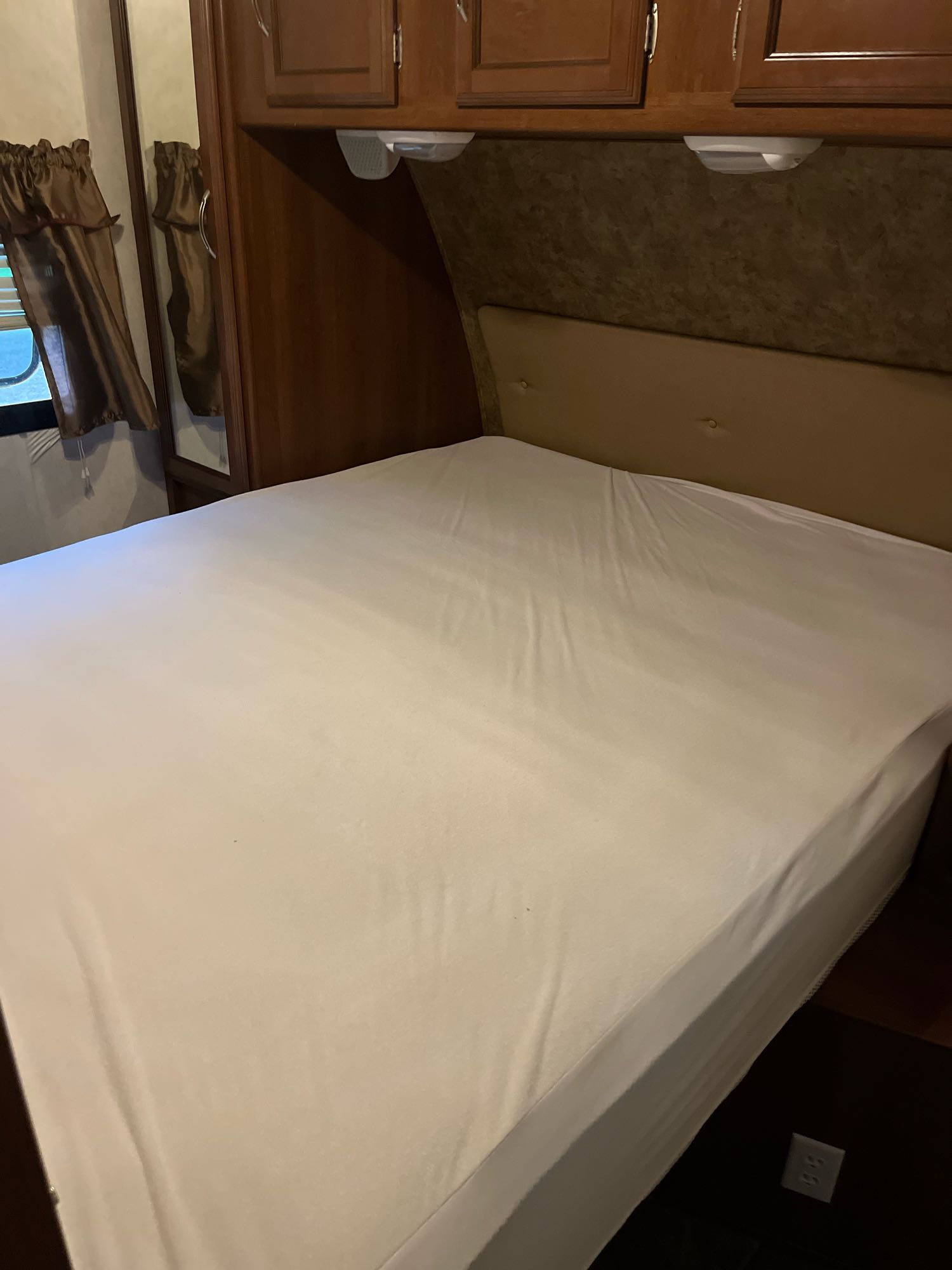 Inside this RV rental's compact bedroom: white-sheeted bed, padded headboard, wooden cabinets, mirror, & window.. ForestRiver Freedom Express 2015