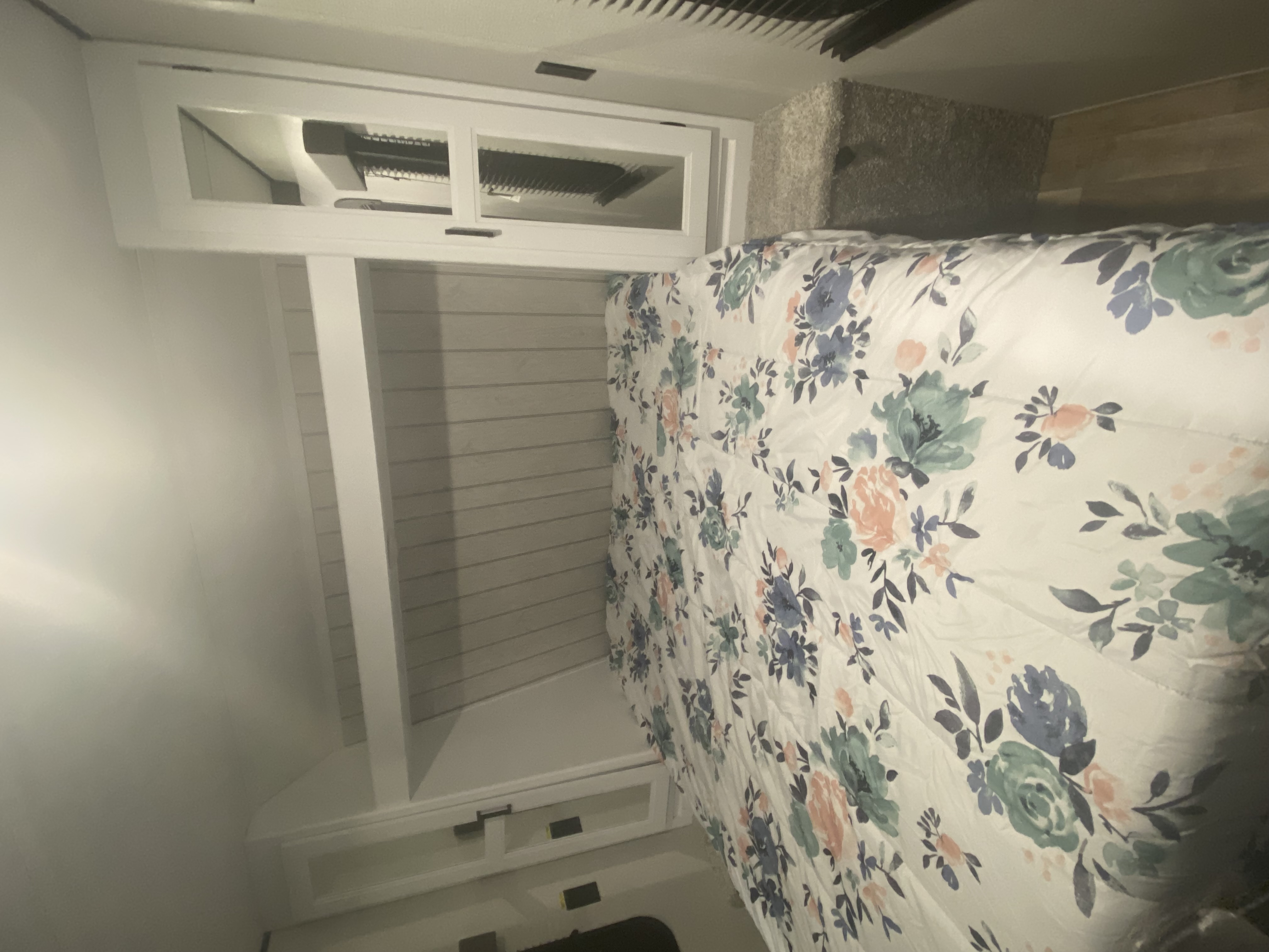 Comfortable RV rental bedroom with a bed, floral comforter, white storage, shiplap wall, and overhead AC unit.. Keystone Hideout 2022