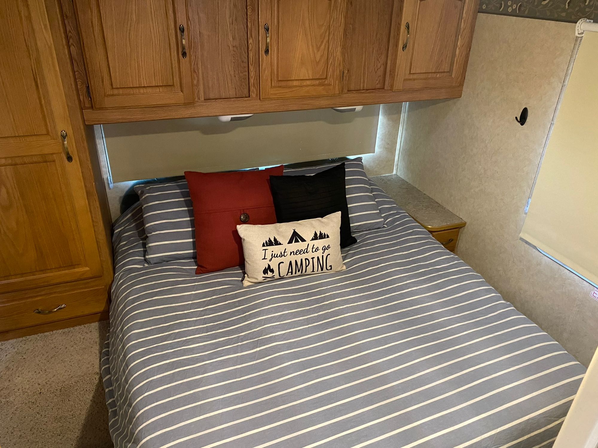 Cozy RV rental bedroom with striped bedding, 'camping' pillow, and overhead wooden cabinets for storage.. Jayco Greyhawk 2006