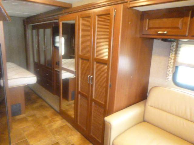 RV rental interior: bedroom/living space featuring a bed, mirrored wooden cabinets, and a light-colored sofa.. Thor Hurricane 2015
