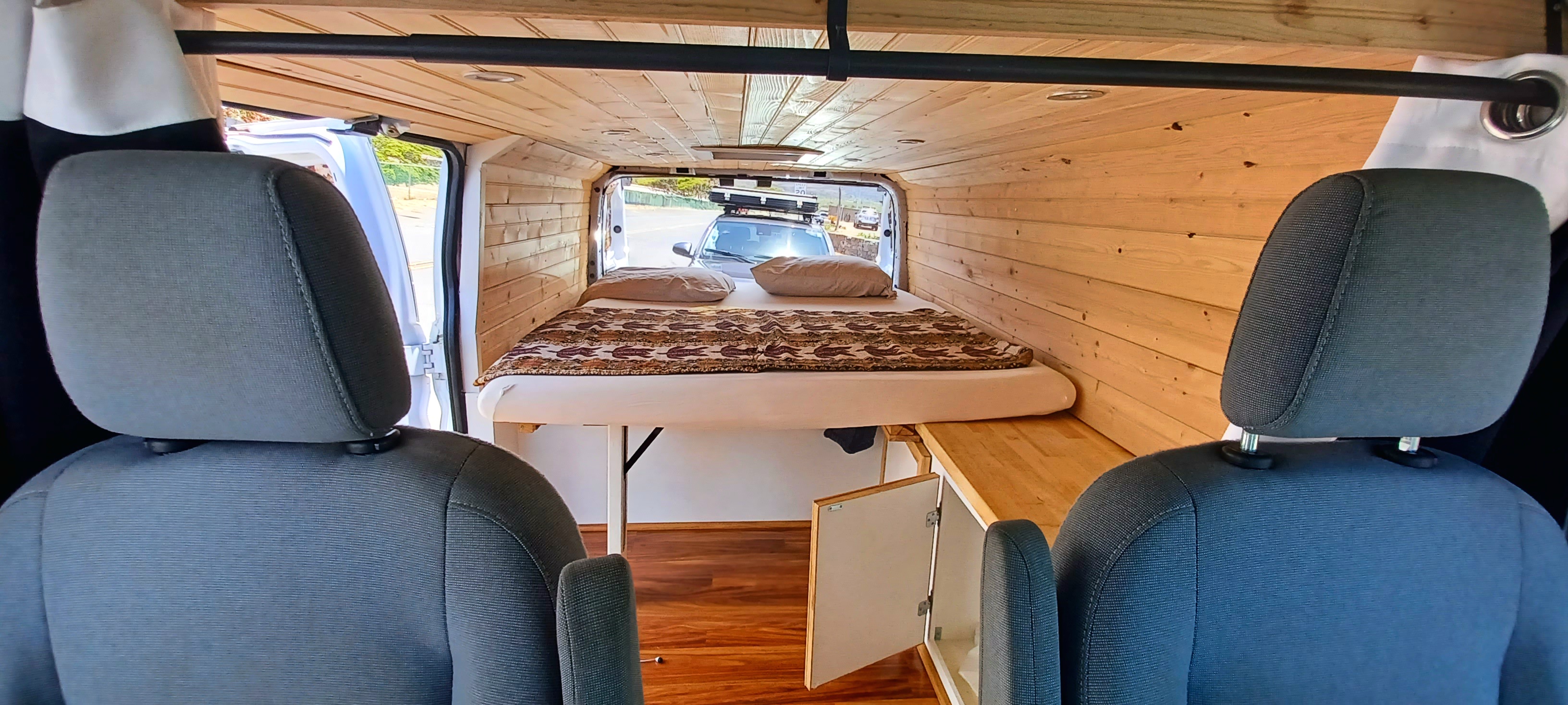 RV rental camper van interior: cozy wood paneling, comfortable bed, and clever storage for your next road trip.. Custom Ford Transit Van 250 2015