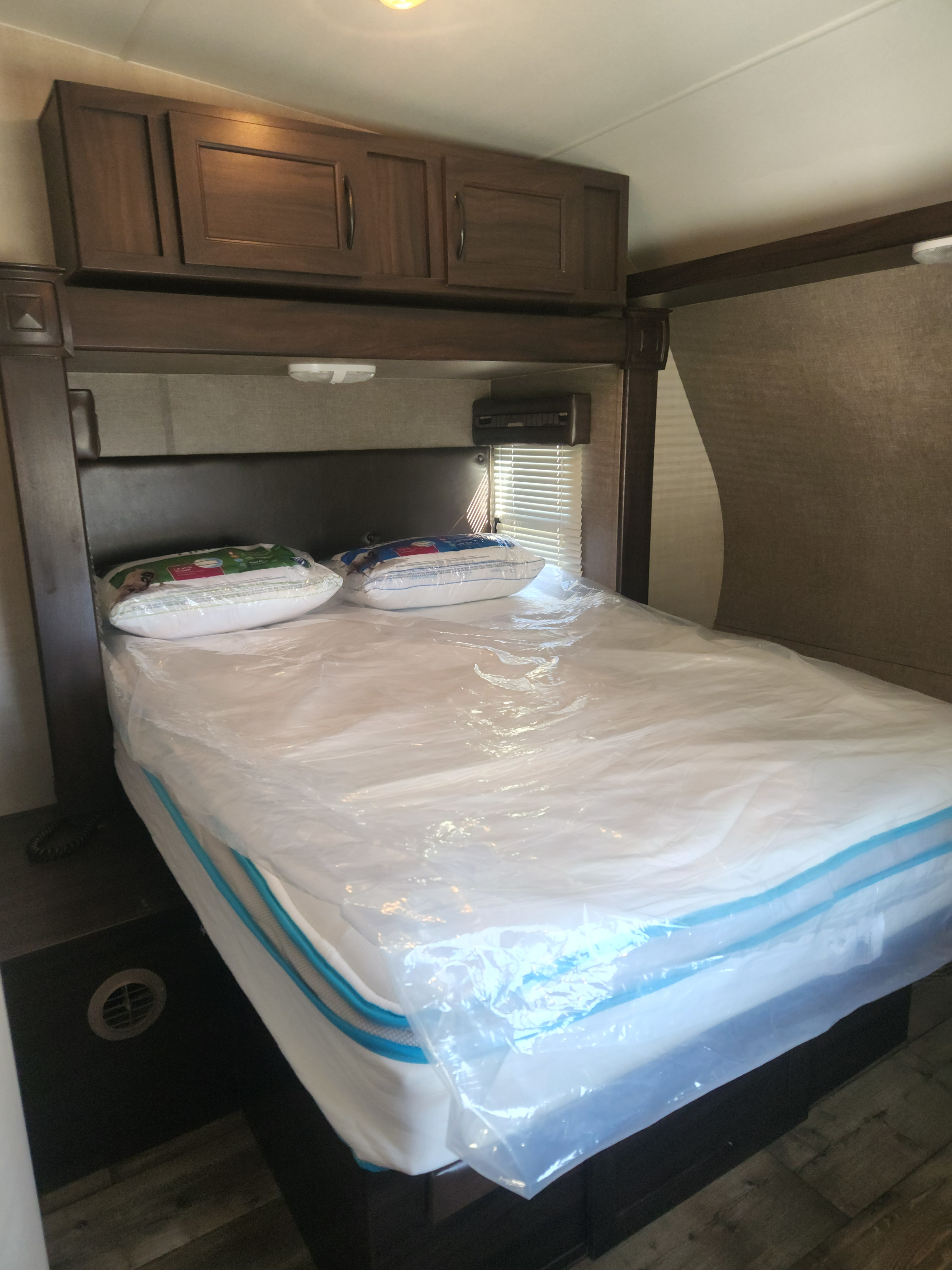 RV rental bedroom with new plastic-wrapped mattress & pillows, wooden cabinets, and window blinds.. Pacific Coachworks Surfside 2018
