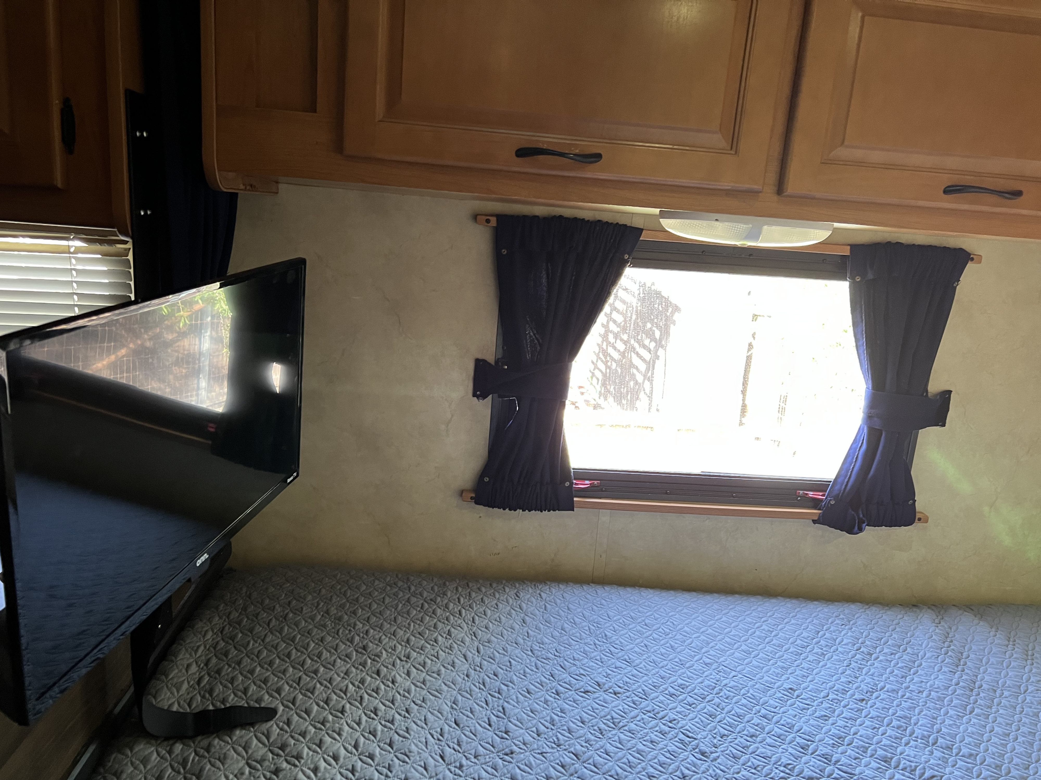 Comfortable RV rental bedroom featuring a quilted bed, TV, wood cabinets, and a window with privacy curtains.. Four Winds Majestic 2011