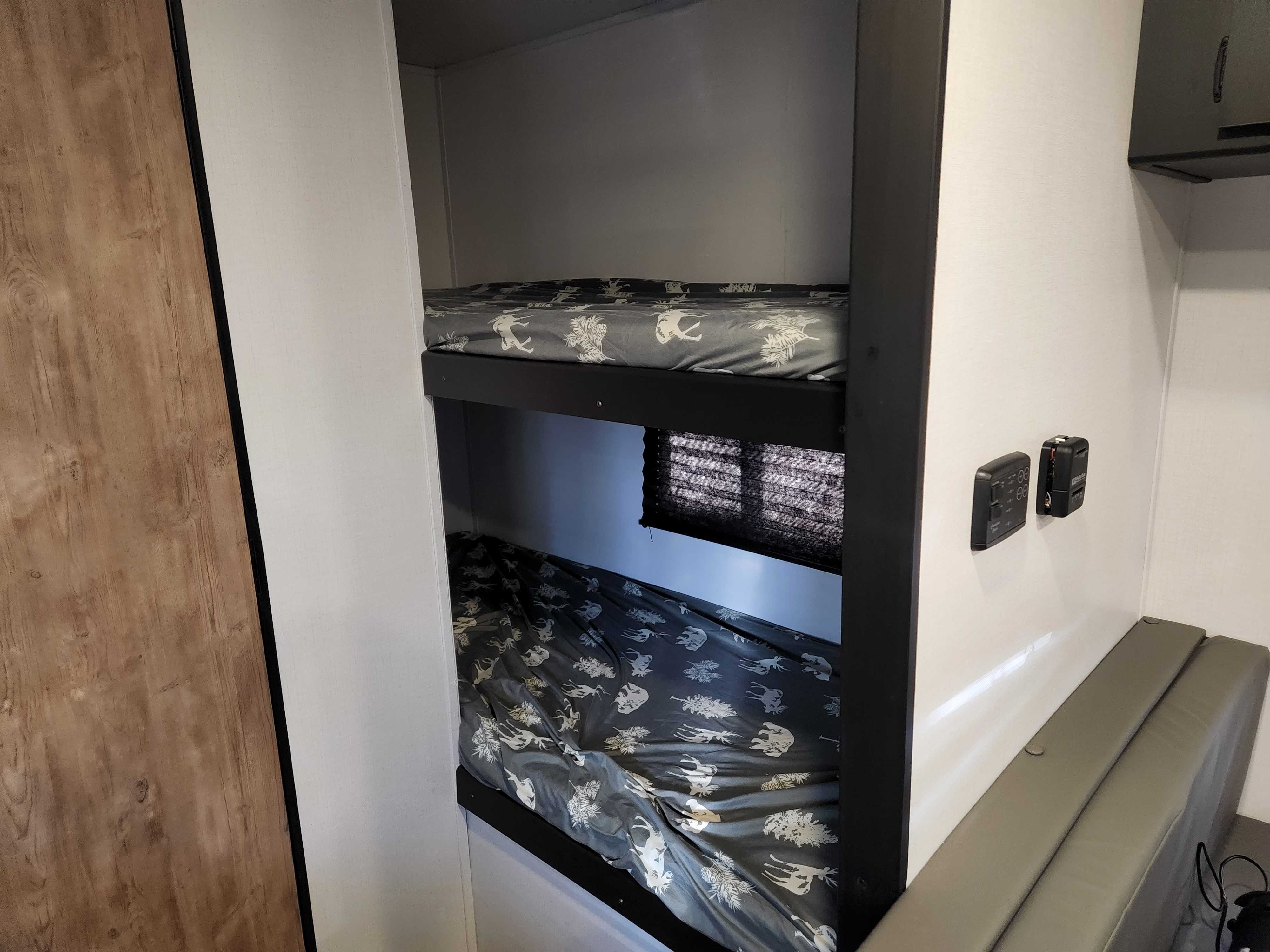 RV rental bunk beds with nature-themed sheets, a window, wall controls, and seating in a compact interior.. Keystone RV Springdale 2022