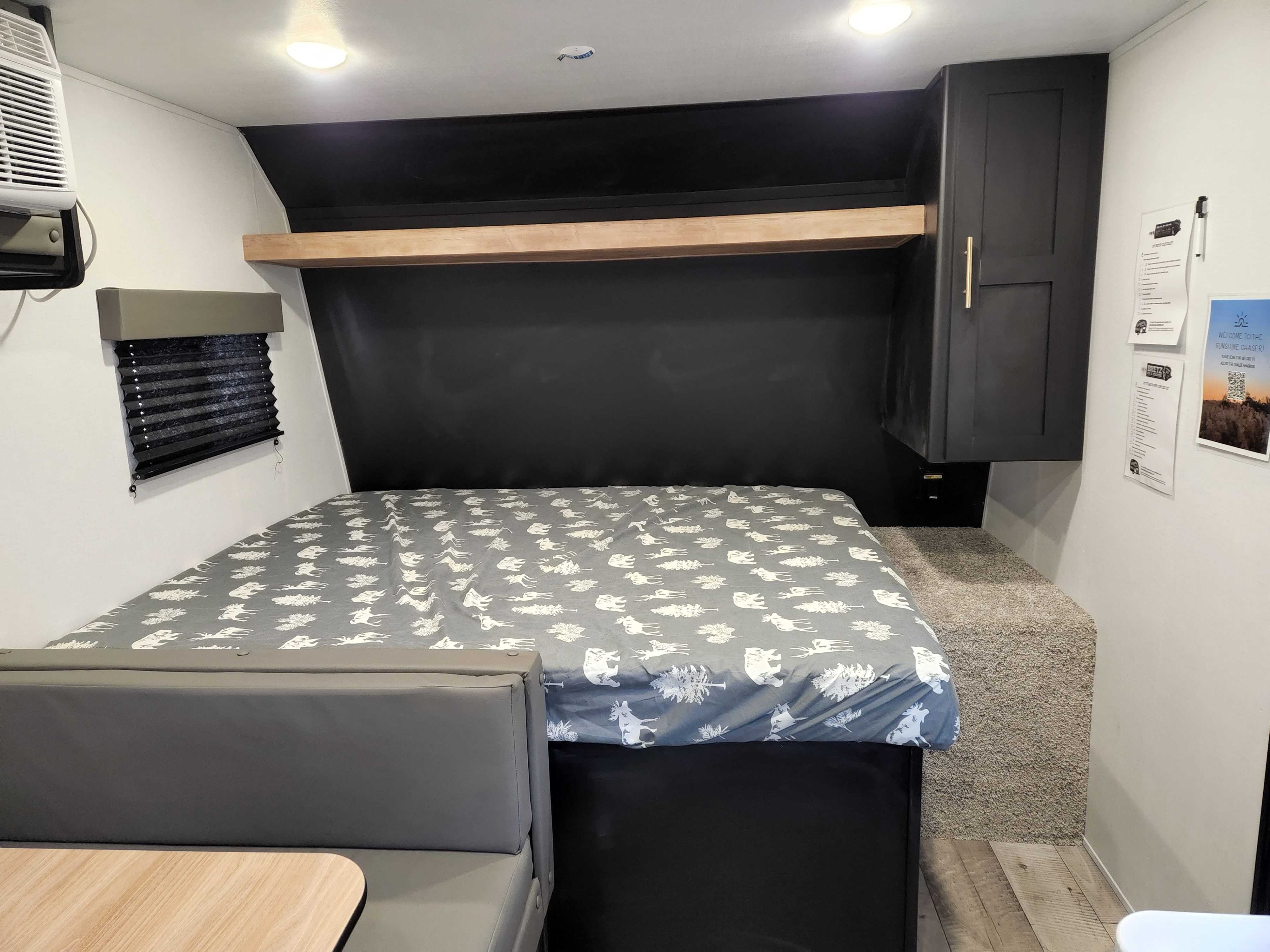 Compact RV rental camper interior: patterned bed, dinette, wall AC, and storage cabinets for travel.. Keystone RV Springdale 2022