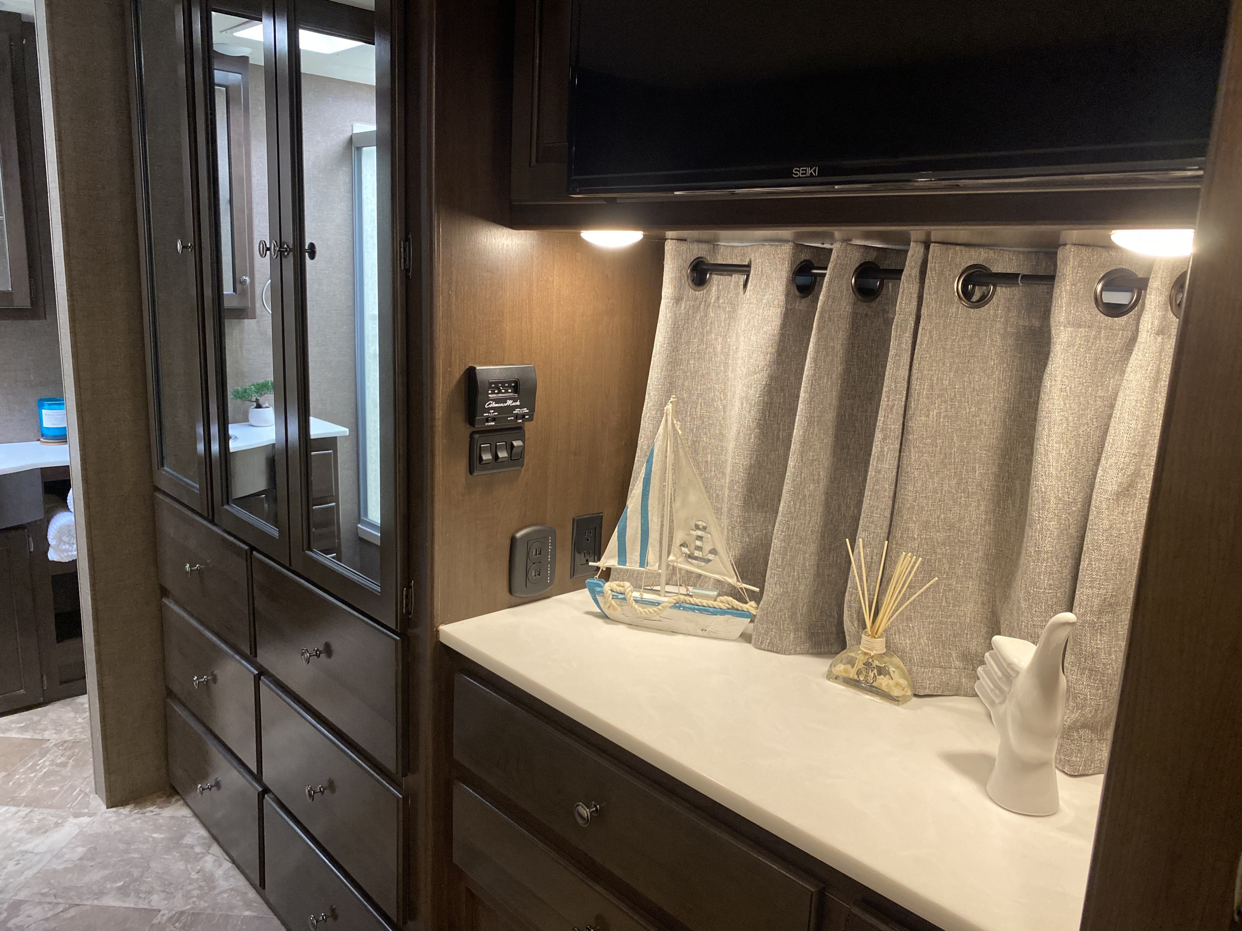 RV rental interior with dark cabinetry, white countertop, sailboat decor, TV, and curtains, reflecting a bathroom area.. Thor Windsport 2017