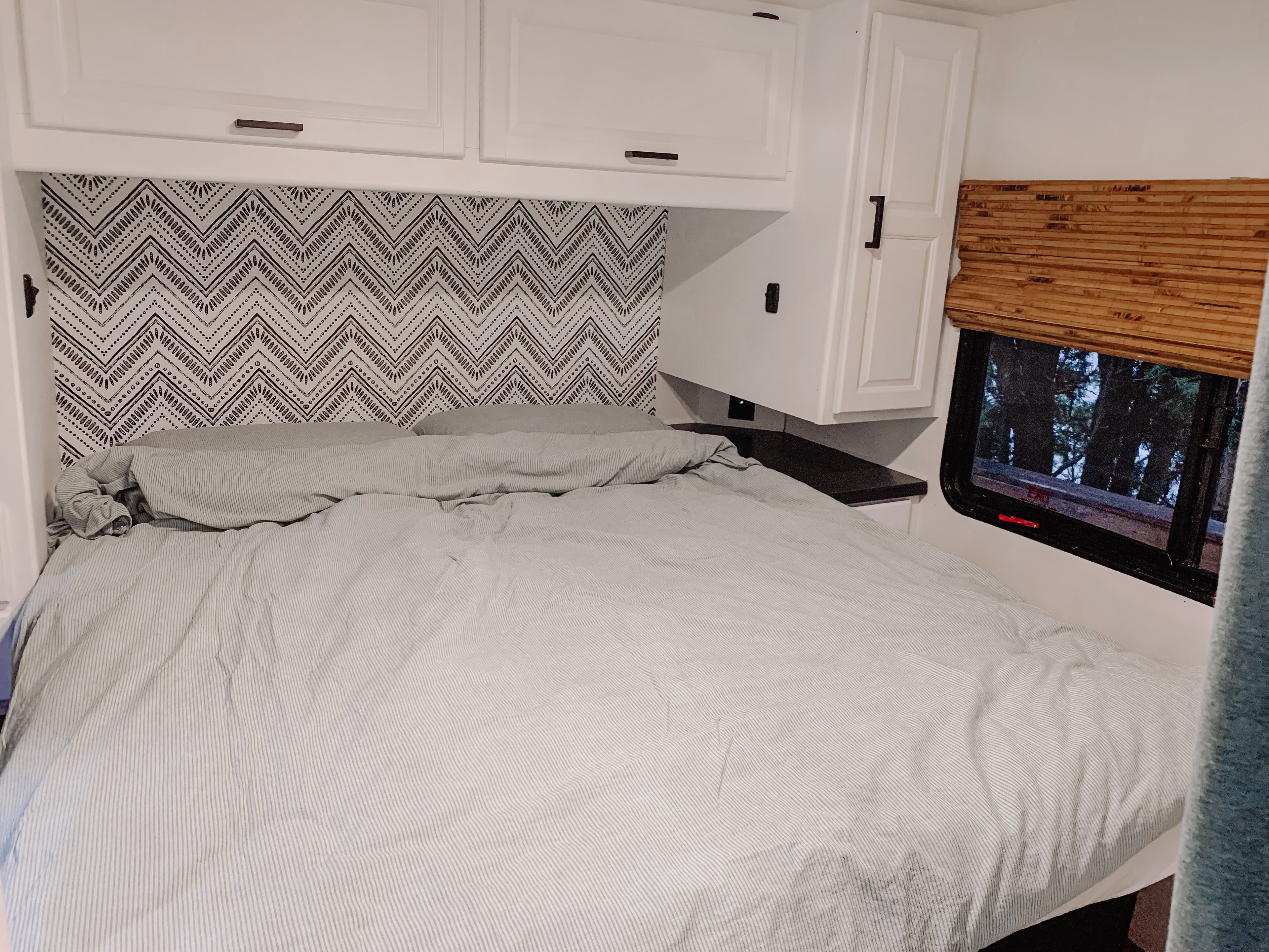 Cozy RV rental bedroom: black & white zigzag wallpaper, striped bed, white cabinets, and a window view.. Thor Majestic 2017