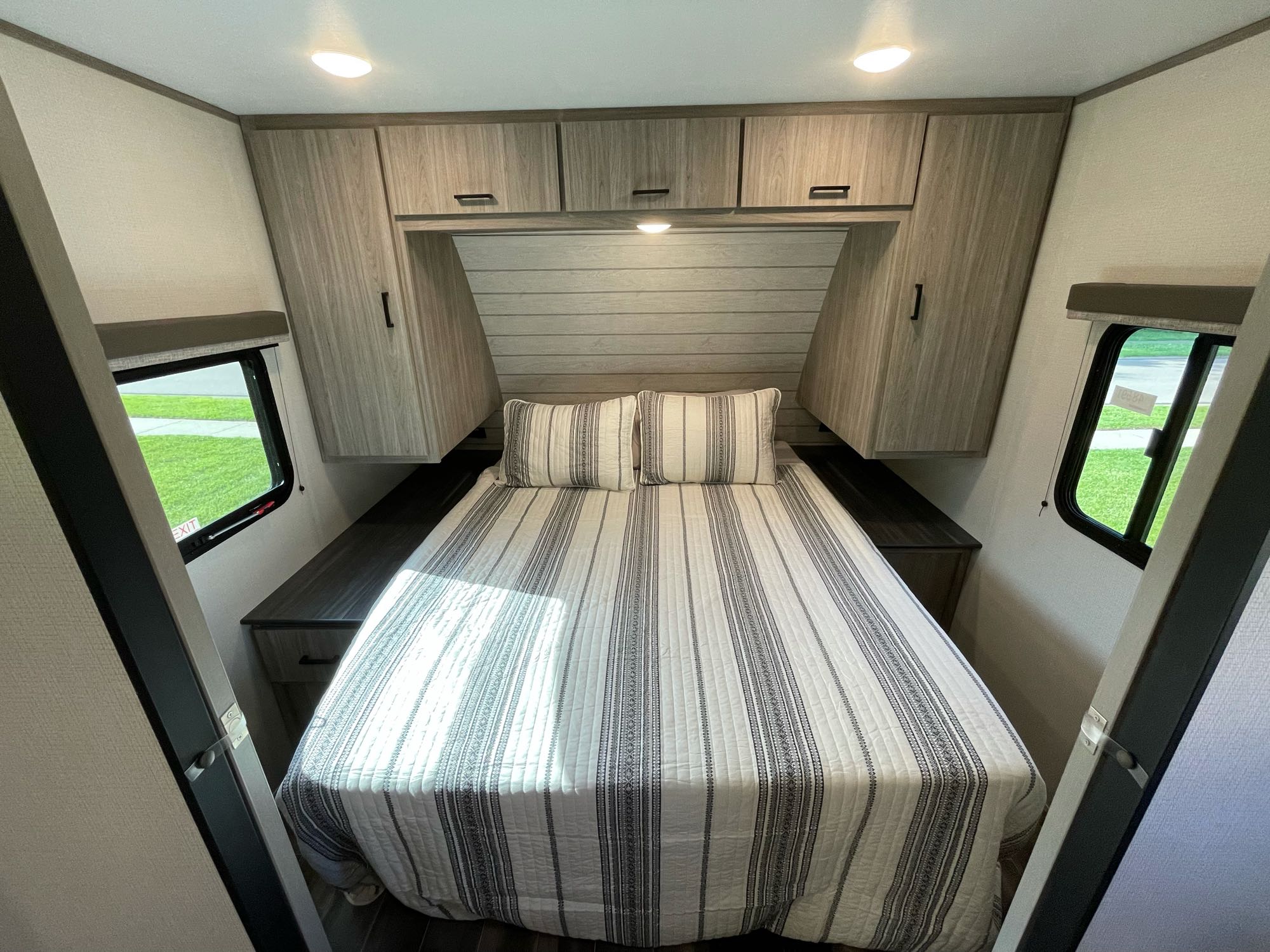 Cozy RV rental bedroom featuring a bed with striped bedding, overhead cabinets, and side windows for a comfortable stay.. Keystone RV Passport SL 2022