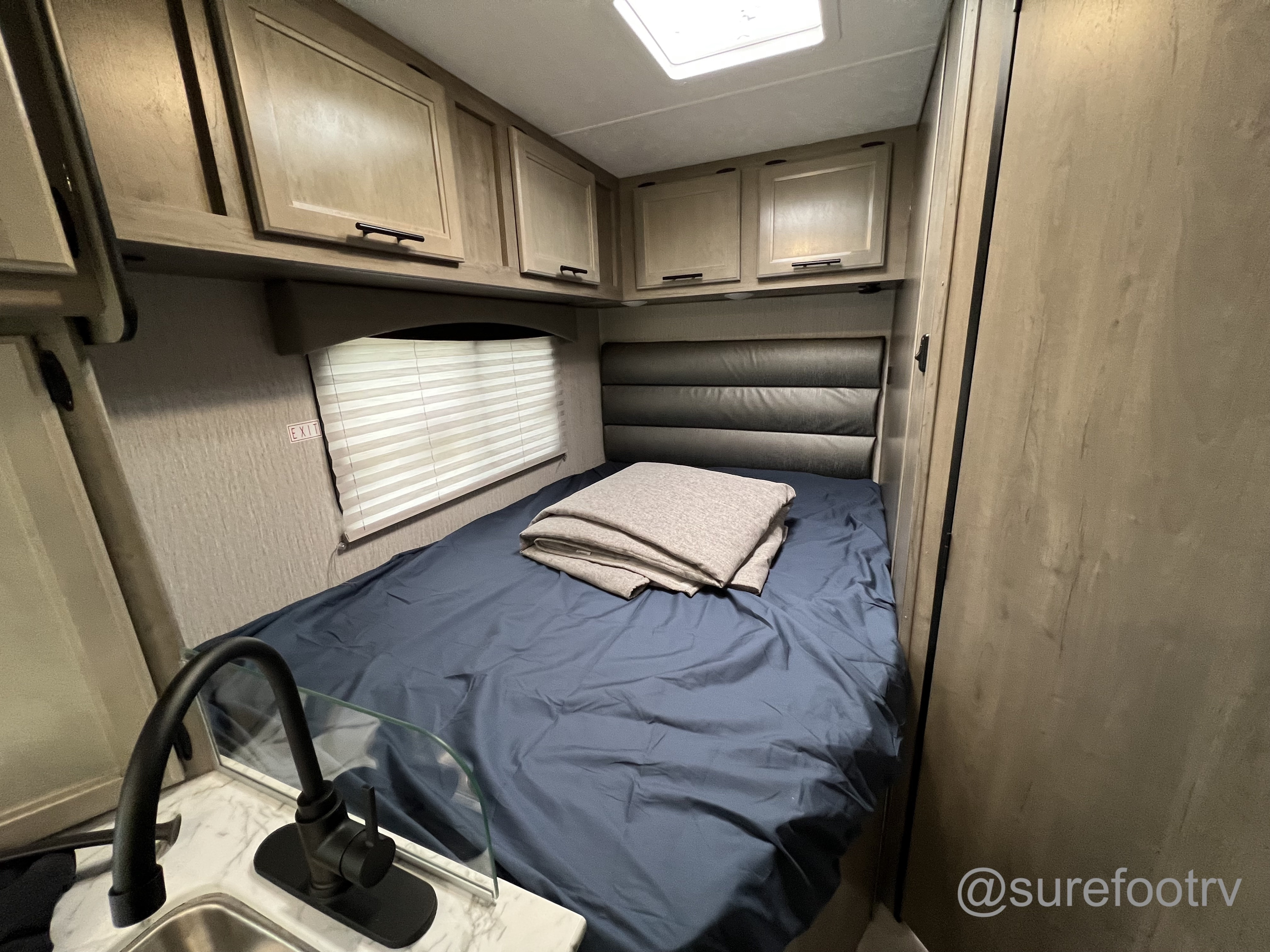 Cozy RV rental interior featuring a bed with blue sheets, overhead cabinets, and a compact kitchen area with sink.. Forest River Coachmen Cross Trail XL 2022