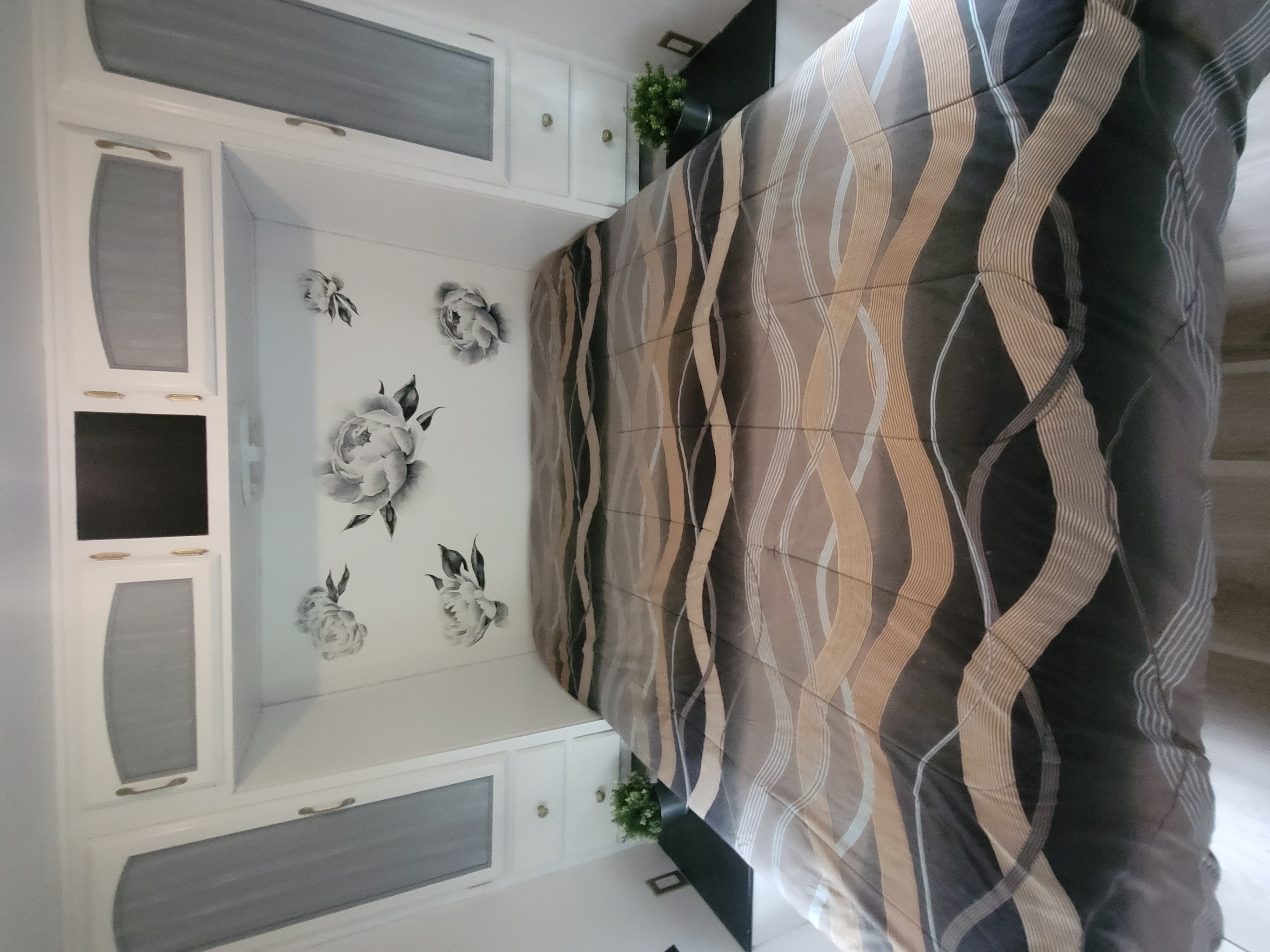 RV rental bedroom featuring a bed with a gray, brown, and white wavy comforter, white cabinets, and floral wall decor.. Forest River Wildwood LE 2009