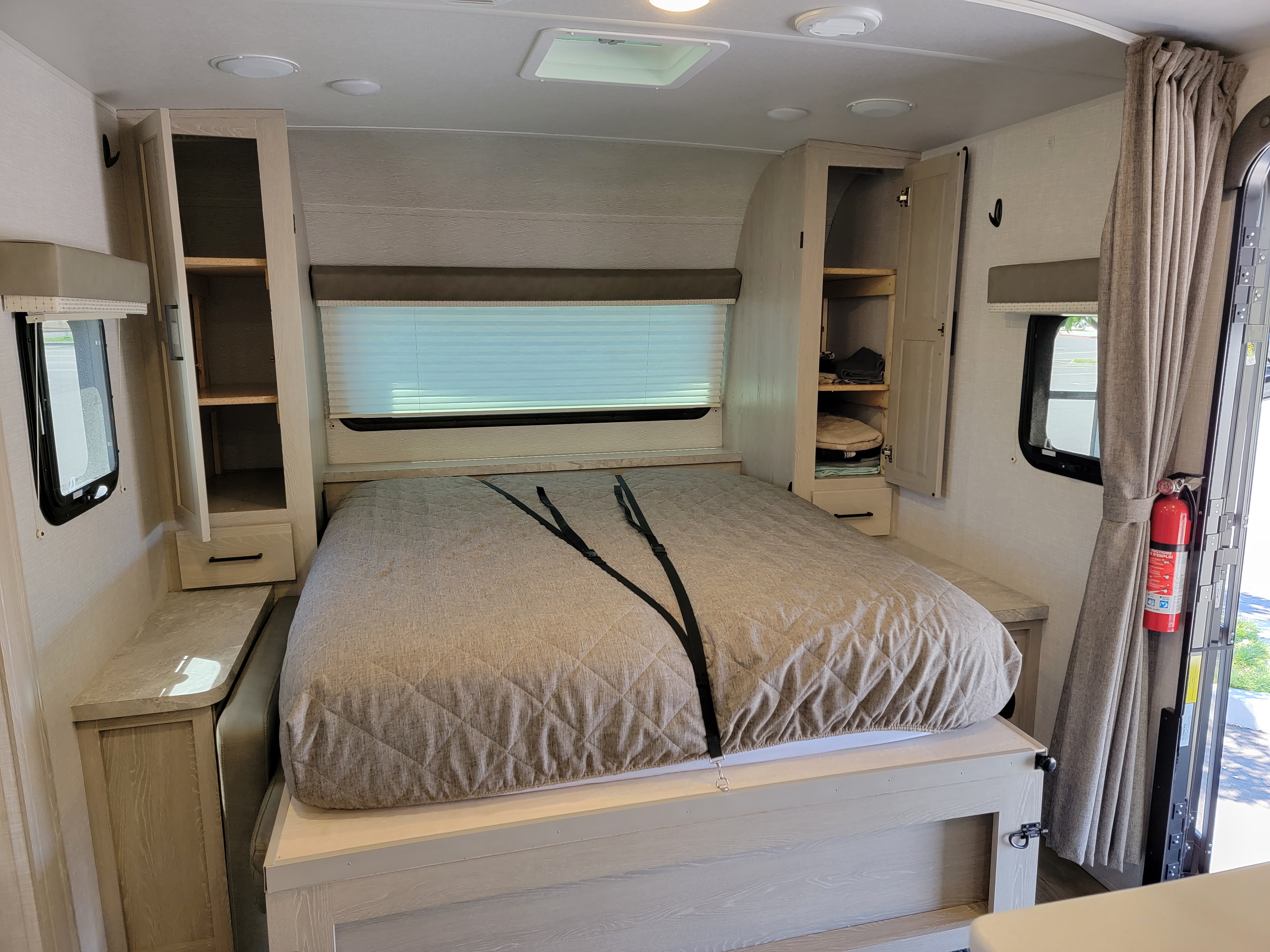 RV rental bedroom: a neat bed with securing straps, built-in storage cabinets, windows, and a fire extinguisher.. Forest River Rockwood Mini Lite 2021