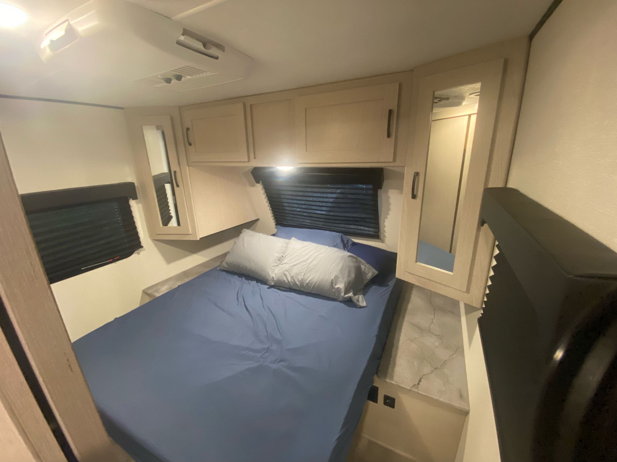 Compact RV rental bedroom with blue bed, overhead cabinets, mirrored storage, and side windows.. Forest River two bedroom Apex ultralite 2022