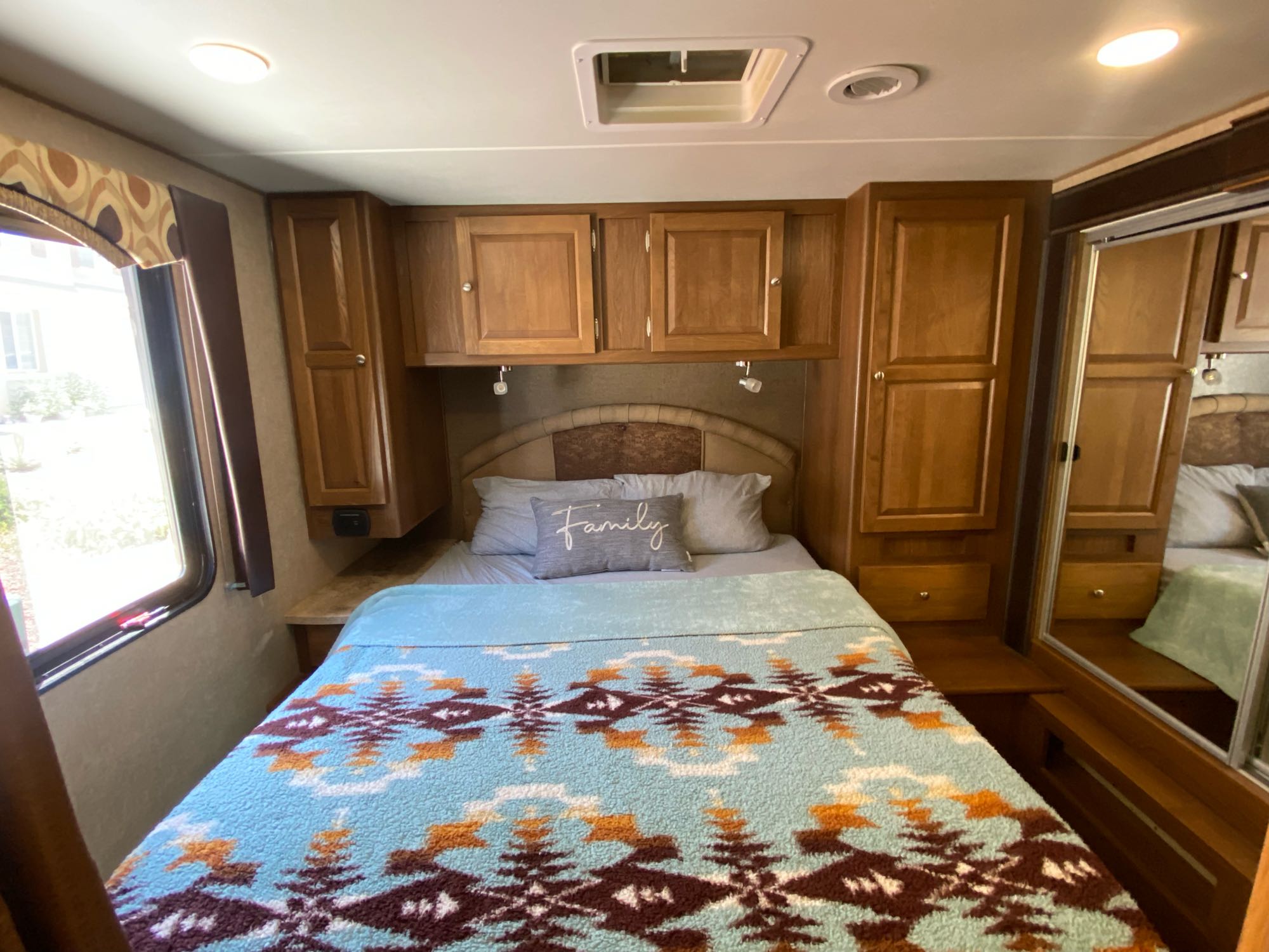 Cozy RV rental bedroom showcasing a bed with a patterned blanket, overhead cabinets, window, and mirrored closet.. Other Other 2017
