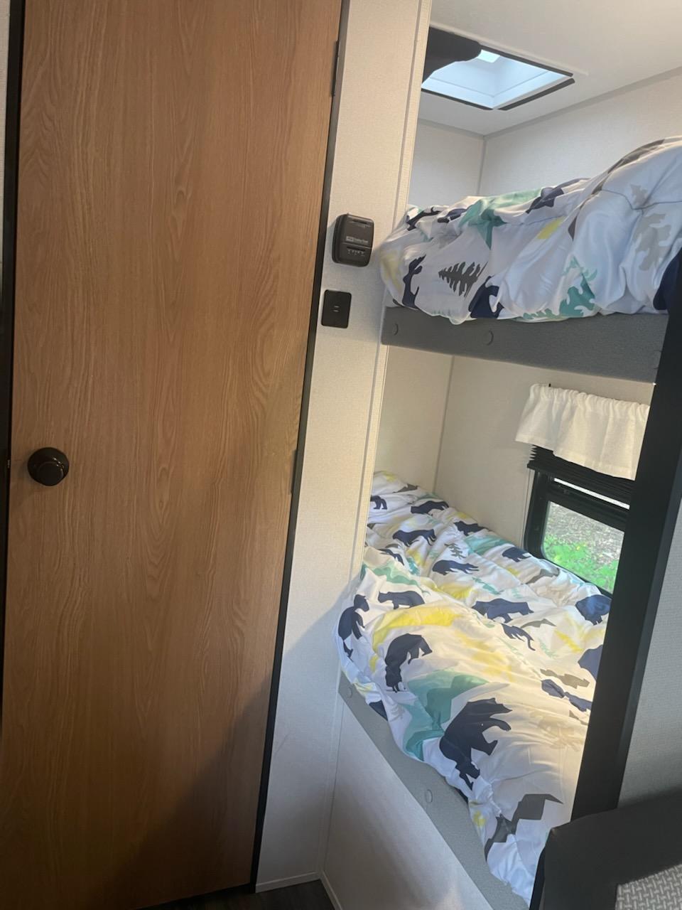 Inside an RV rental: cozy bunk beds with bear-themed bedding, a skylight, and a nature view from the window.. Prime Time Avenger 2022