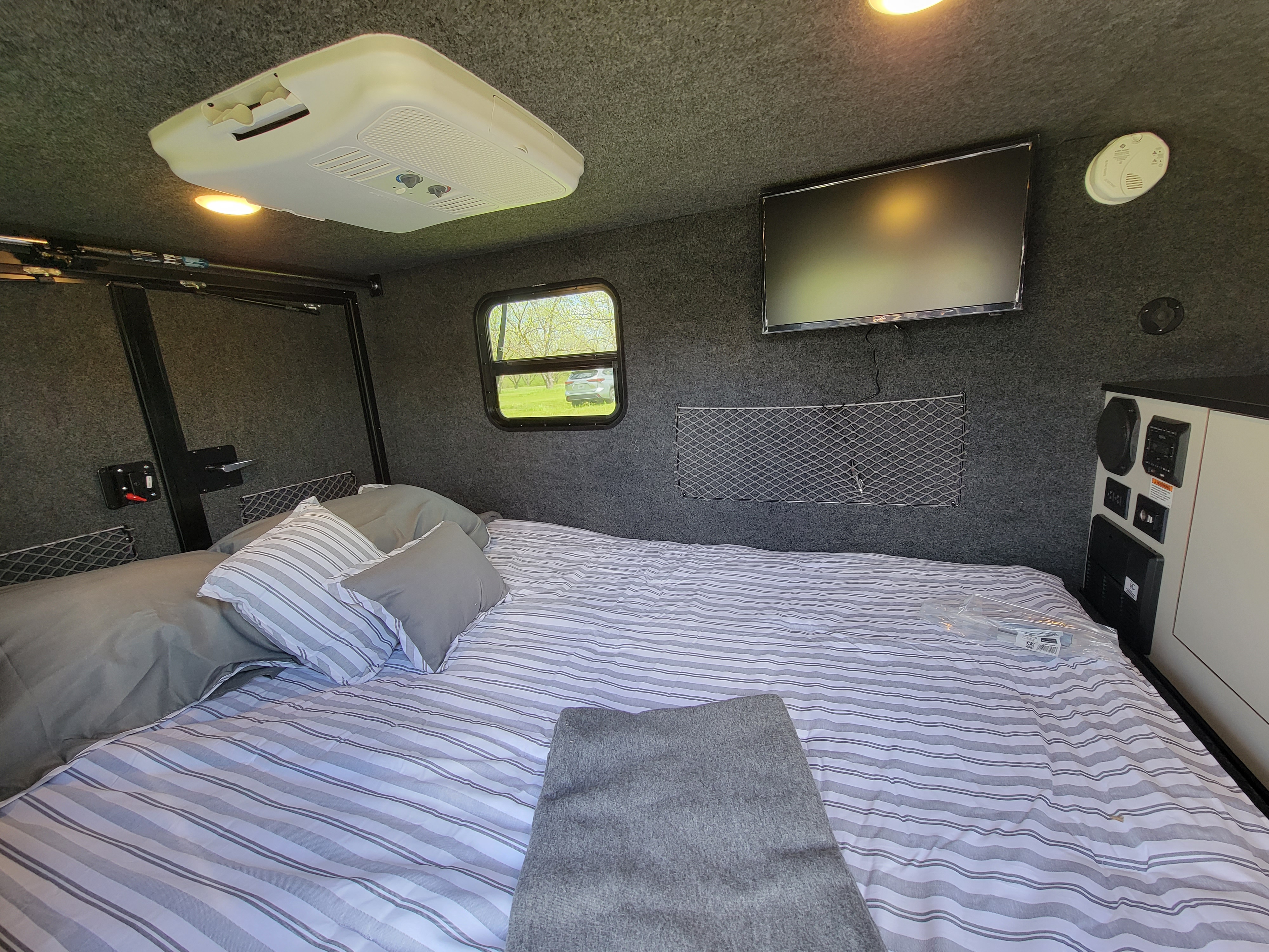 Cozy RV rental interior with a spacious bed, mounted TV, AC unit, and window views.. InTech RV InTech RV Trailer 2021