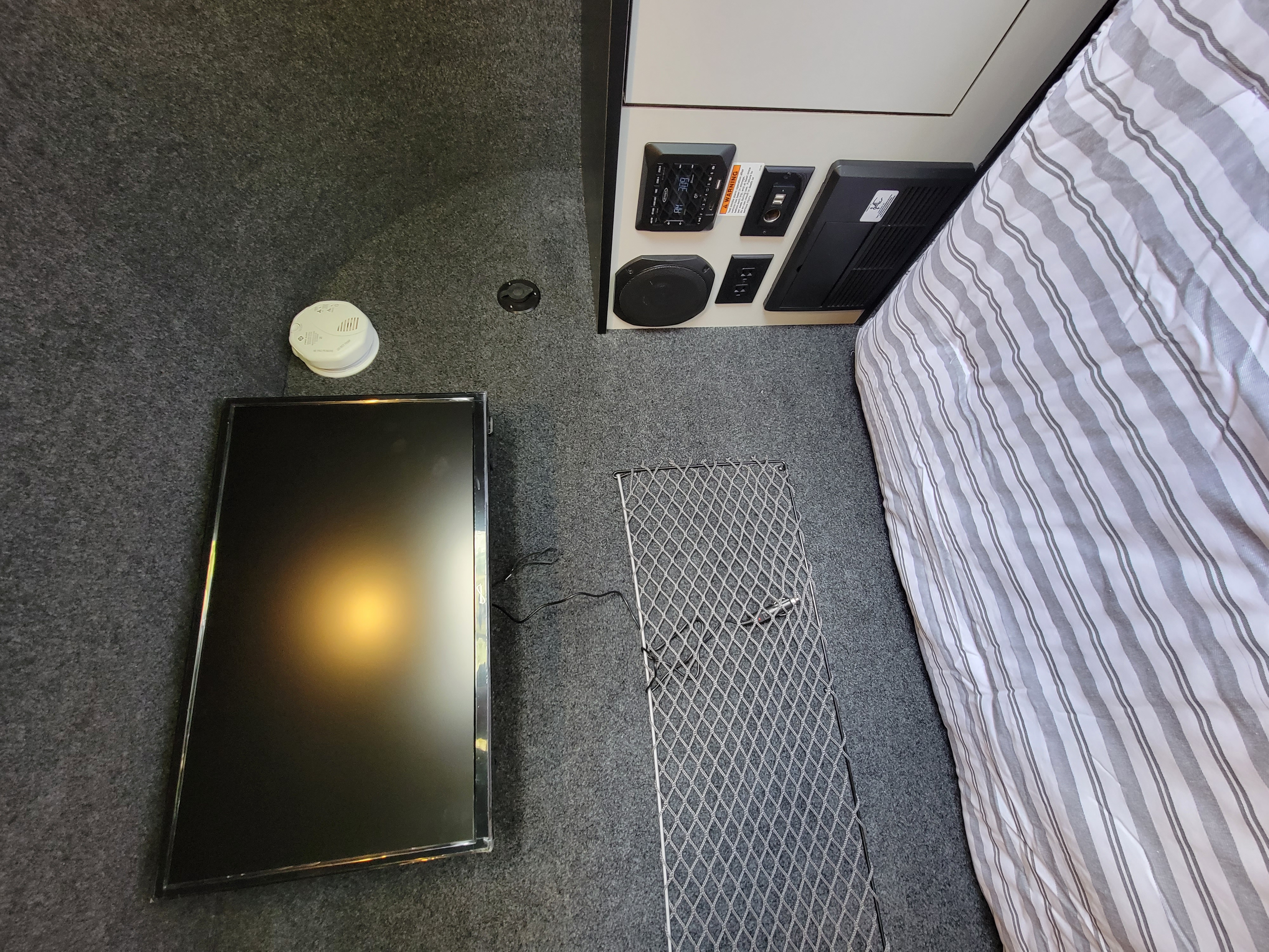 RV rental interior: TV, bed, smoke detector, and amenities control panel on gray carpet with mesh mat.. InTech RV InTech RV Trailer 2021
