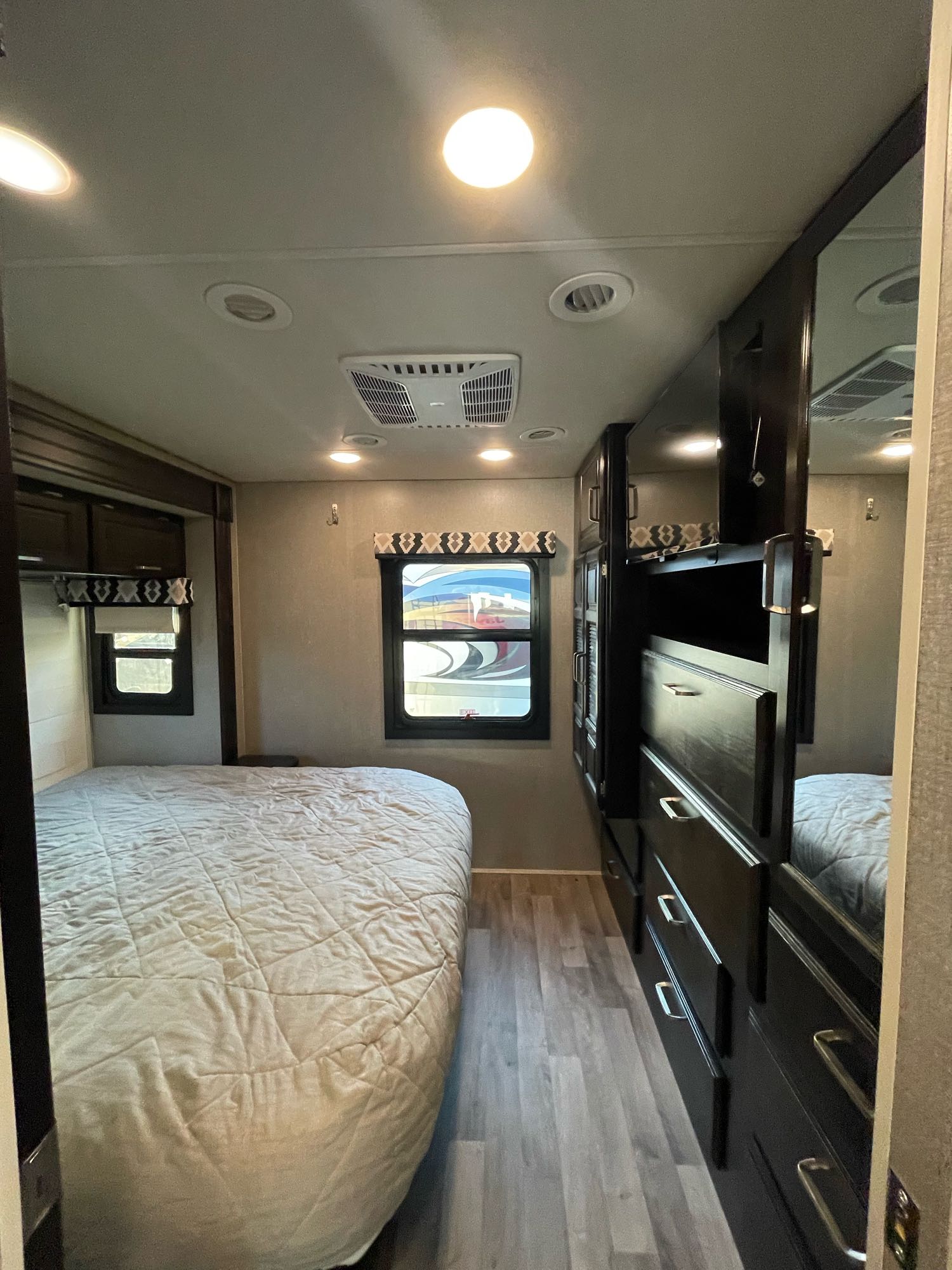 Compact RV rental bedroom with a comfortable bed, dark wood dresser, and windows, showcasing its modern interior.. Jayco Precept 2021