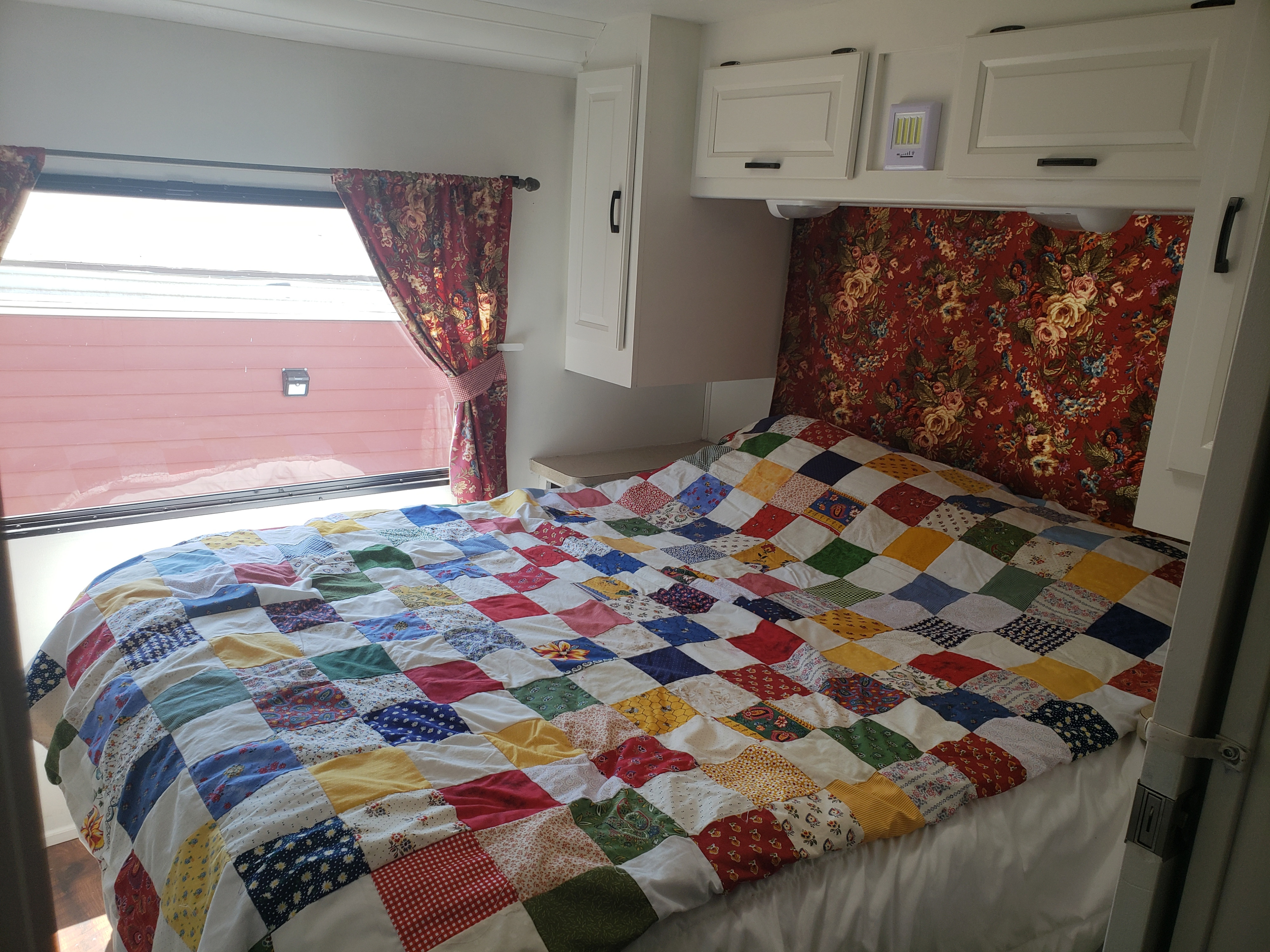 Cozy rv rental bedroom featuring a colorful patchwork quilt, matching floral curtains, and white overhead cabinets.. Forest River Sunseeker 2014