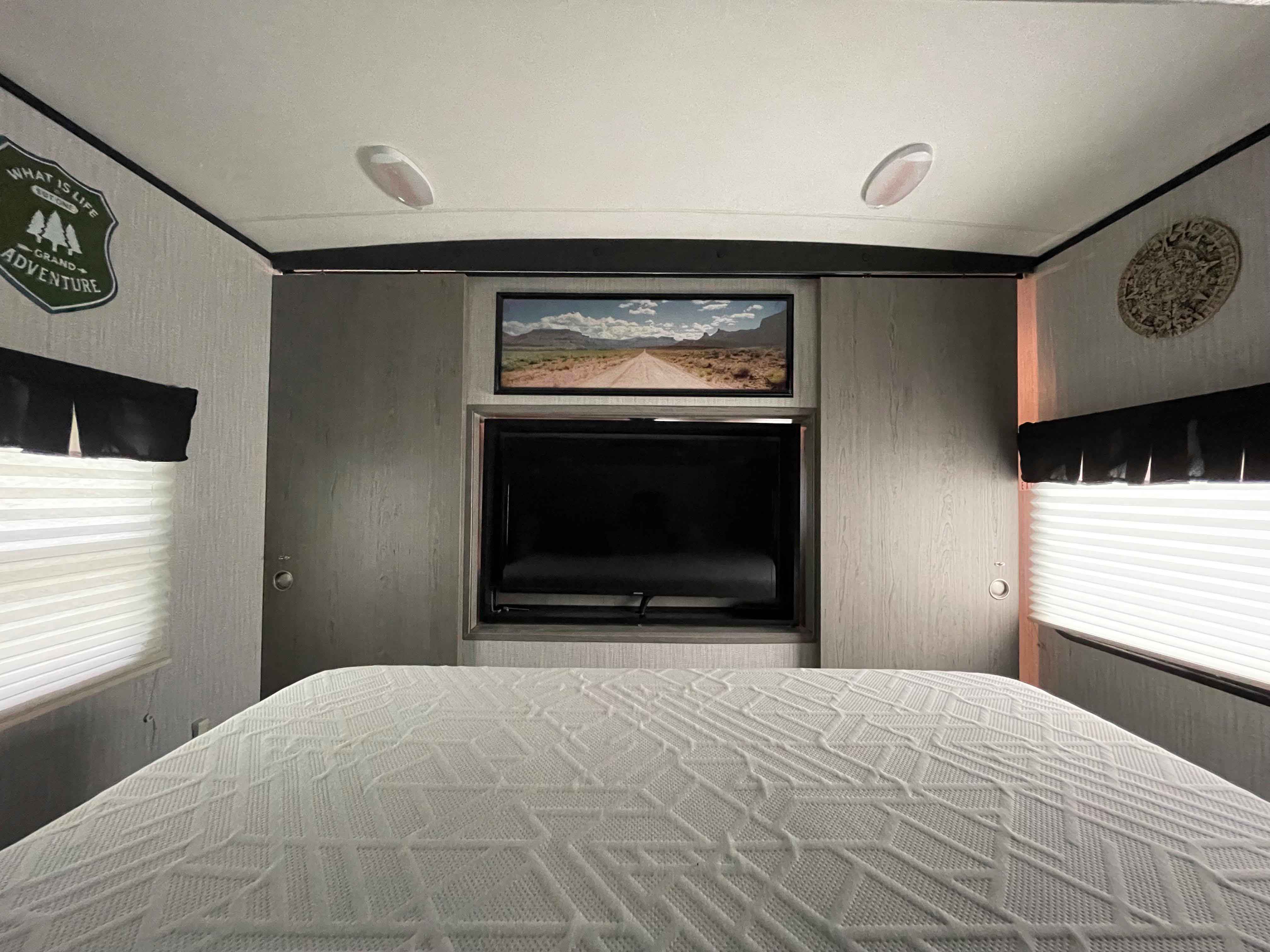 Inside a cozy RV rental bedroom, featuring a comfortable bed, mounted TV, and adventure-themed wall art.. Heartland RVs Mallard 2021