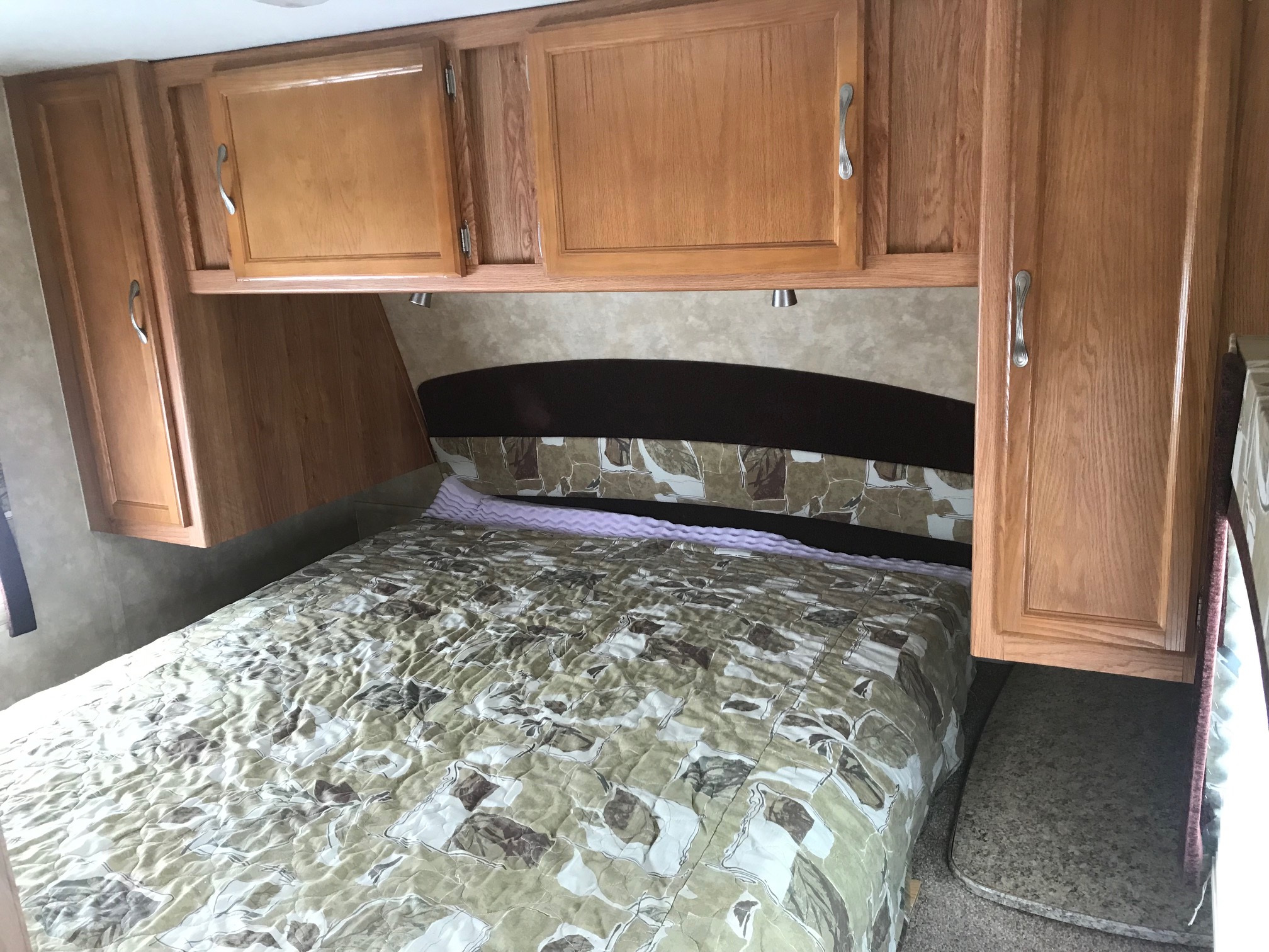 Cozy RV rental bedroom with a comfy bed, overhead wooden cabinets, and a padded headboard.. Jayco Jay Feather 2010