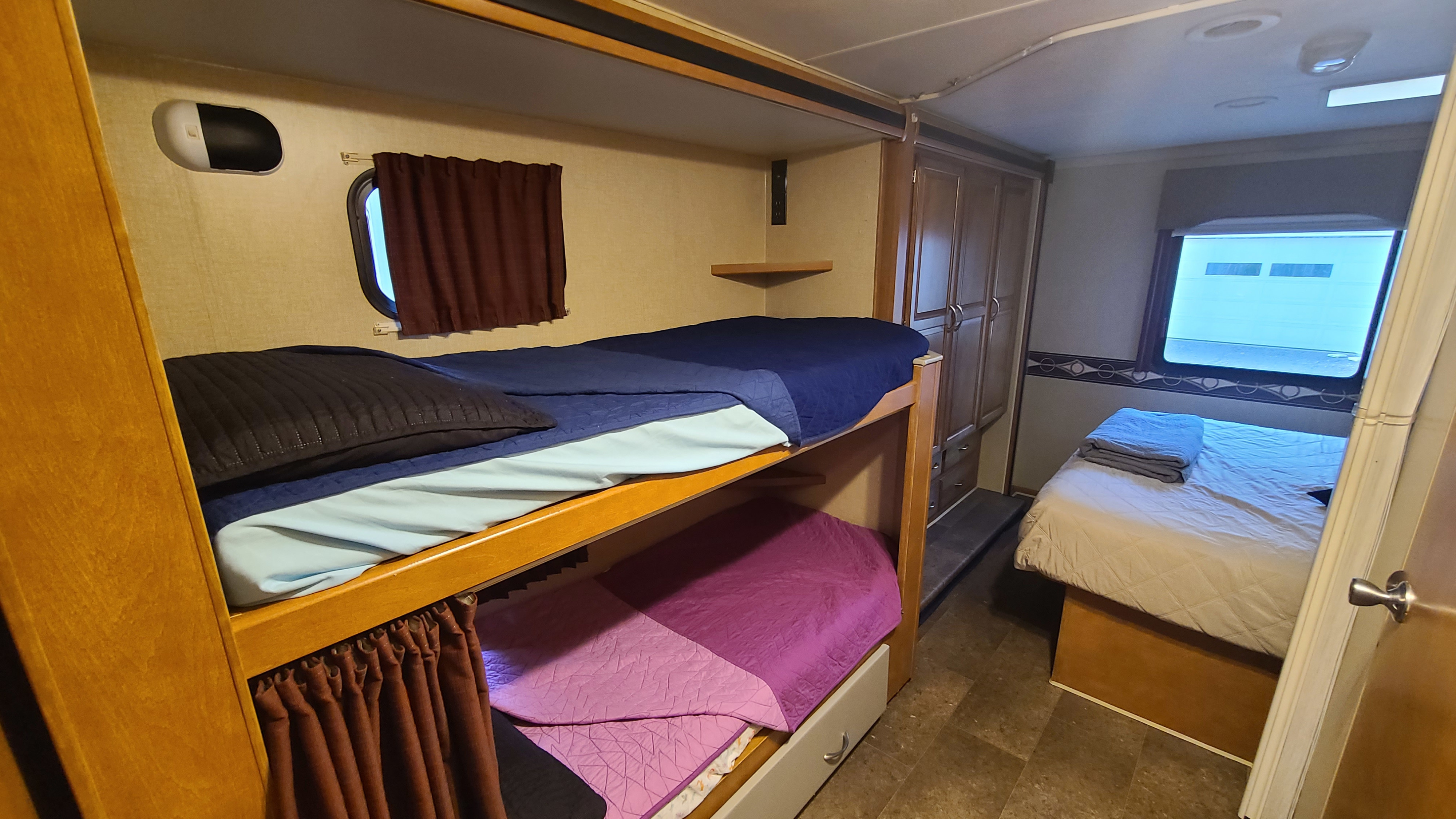 Cozy RV rental interior featuring bunk beds with blue/purple bedding, a master bed, and storage cabinetry.. Winnebago Minnie Winnie 2017