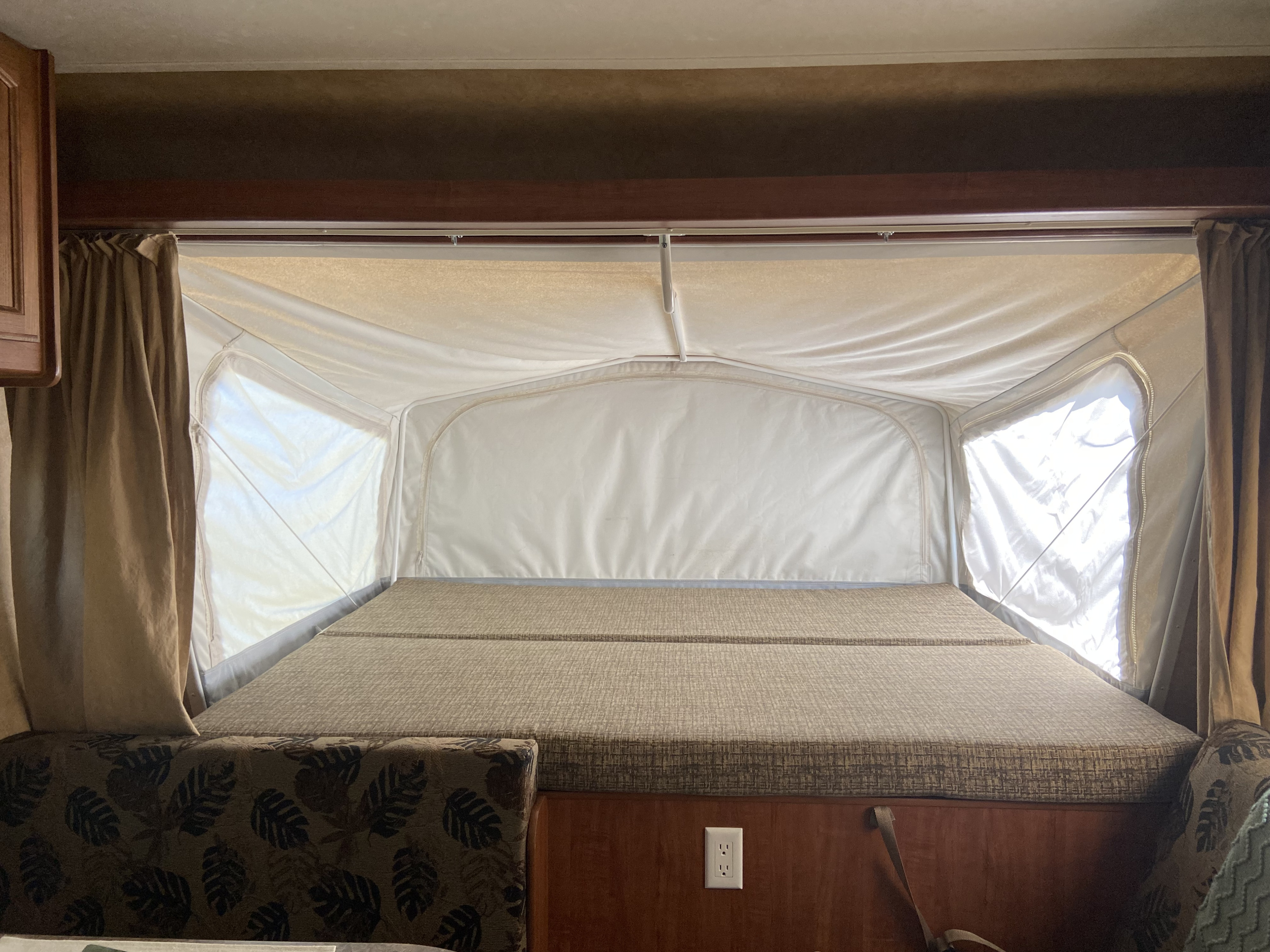 Inside an RV rental: a spacious pop-up bed with patterned cushions, surrounded by canvas walls and windows.. Jayco Jay Feather Sport EXP 2011