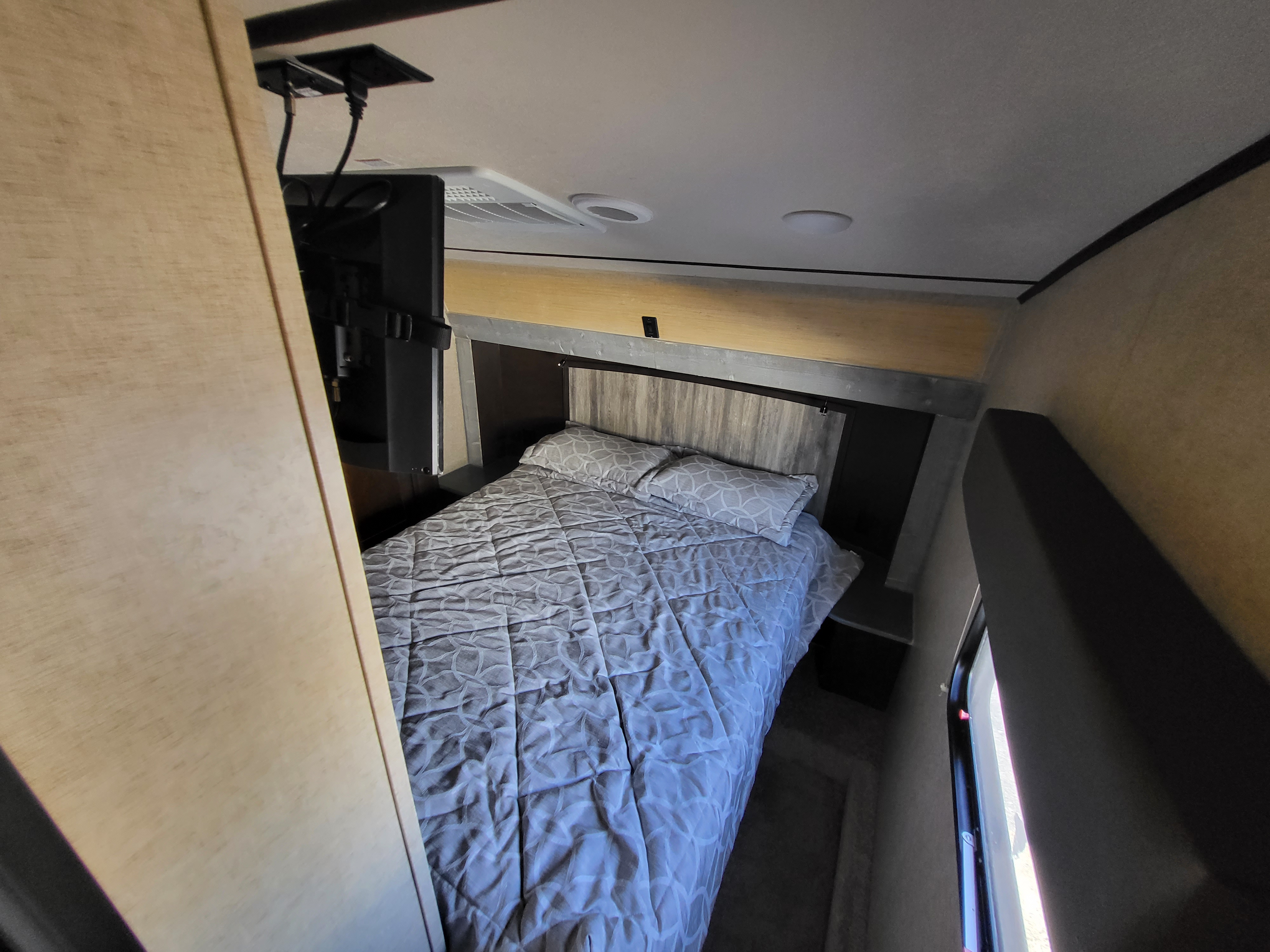 RV rental bedroom features a comfy bed with patterned comforter, wall-mounted TV, and overhead AC unit.. Forest River Cherokee Arctic Wolf 2018
